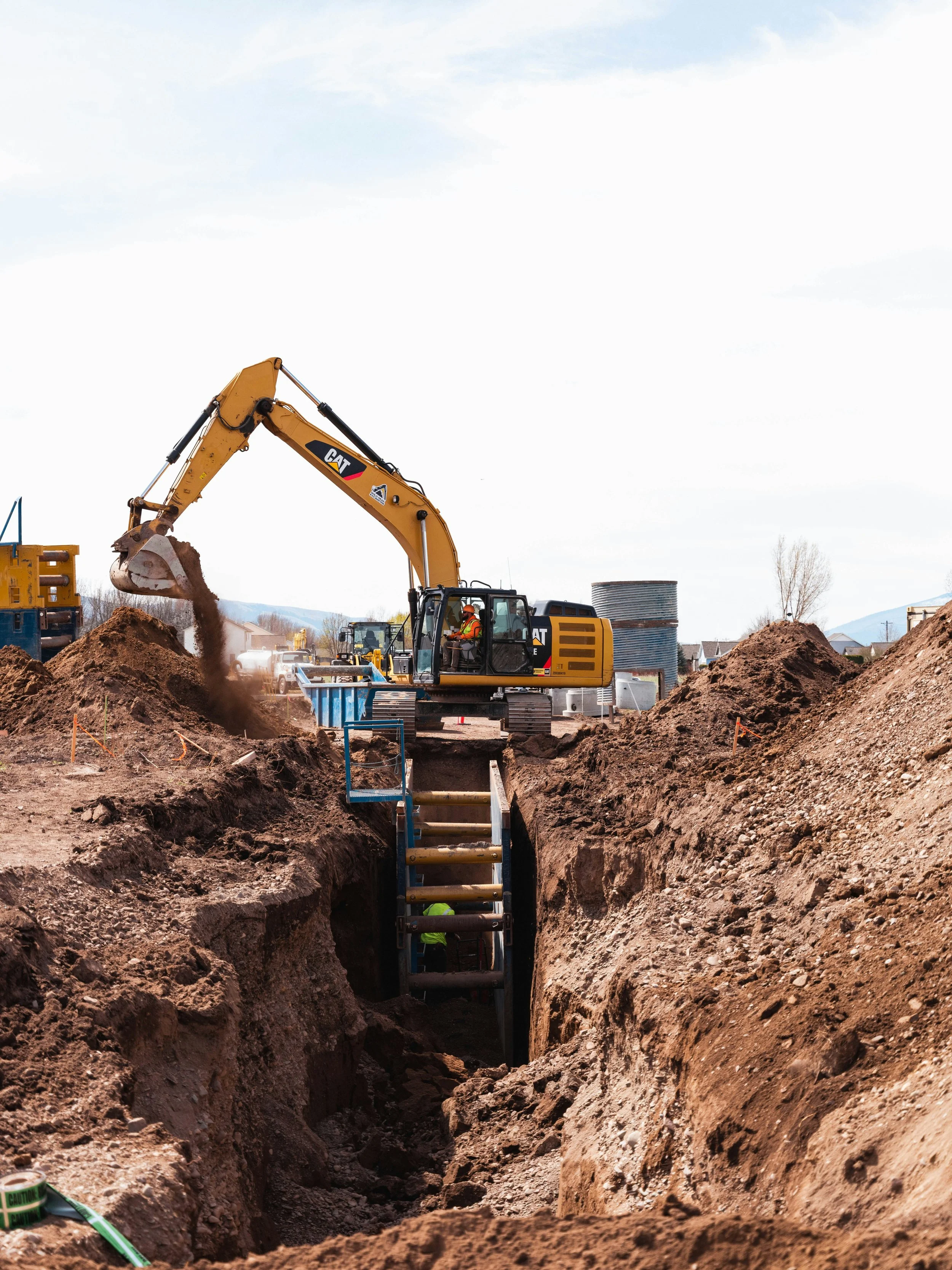 Excavator digging a trench at a construction site with workers and construction materials.