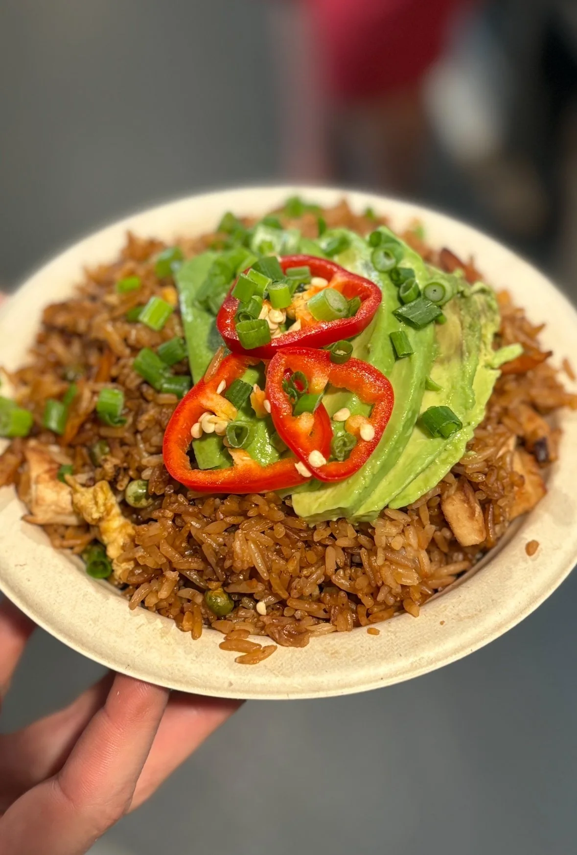 A bowl of fried rice topped with sliced red chili peppers, sliced avocado, and chopped green onions.