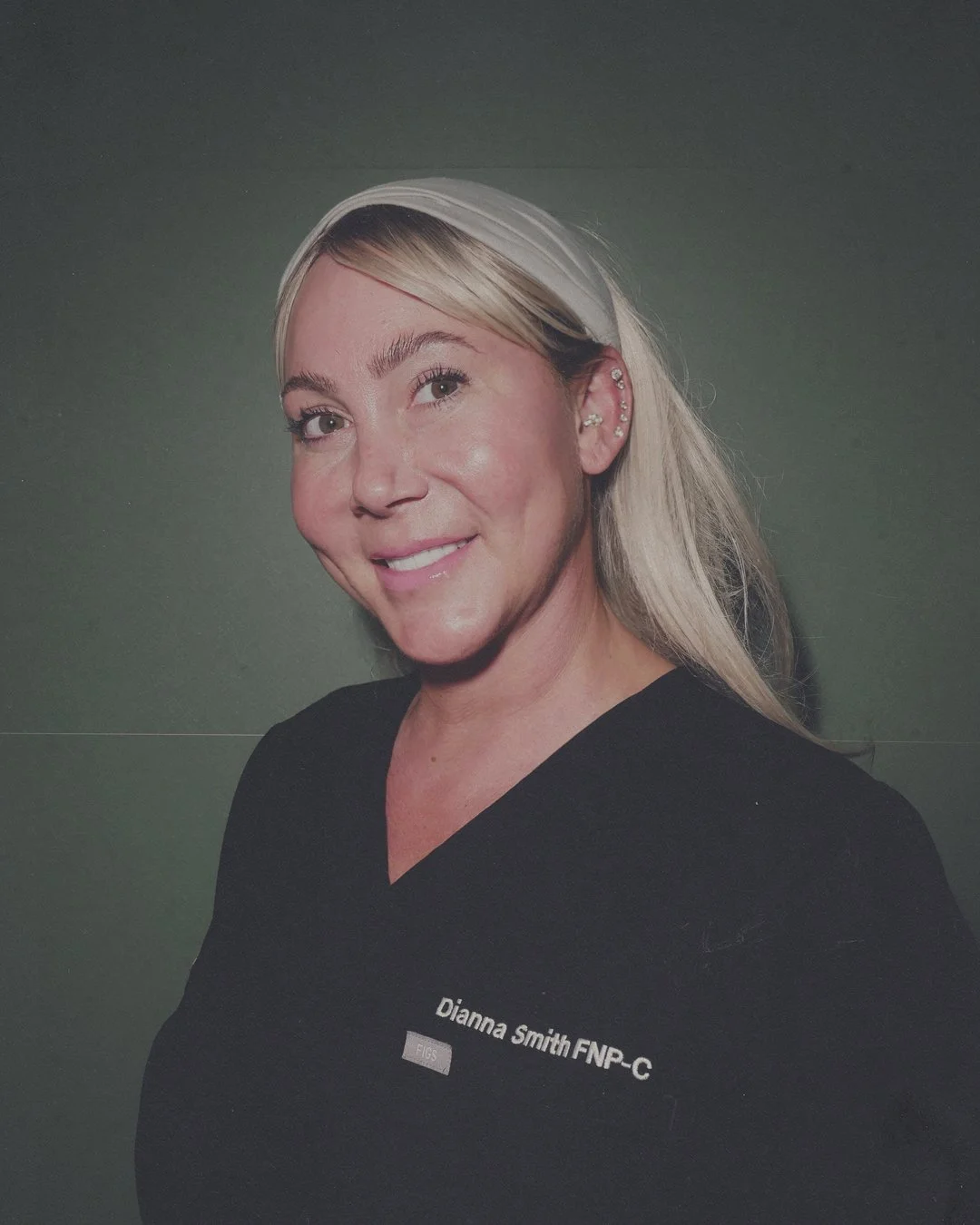 Portrait of a woman with blonde hair wearing a black shirt with a name tag that reads 'Dianna Smith FNP-C,' smiling and standing against a green background.