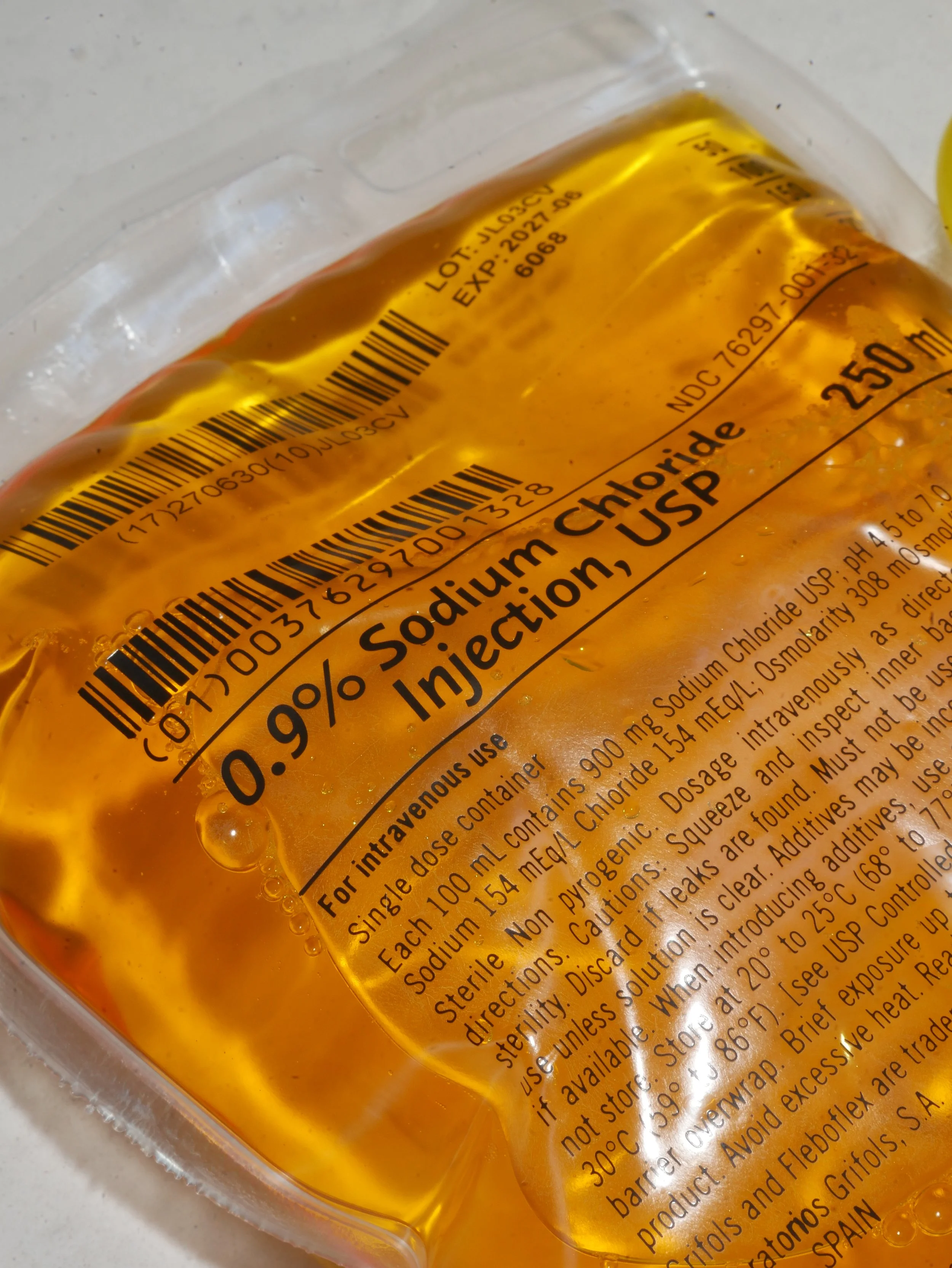 A bag of injectable sodium chloride solution with a yellow liquid, labeled for intravenous use, with barcode and instructions on the label.