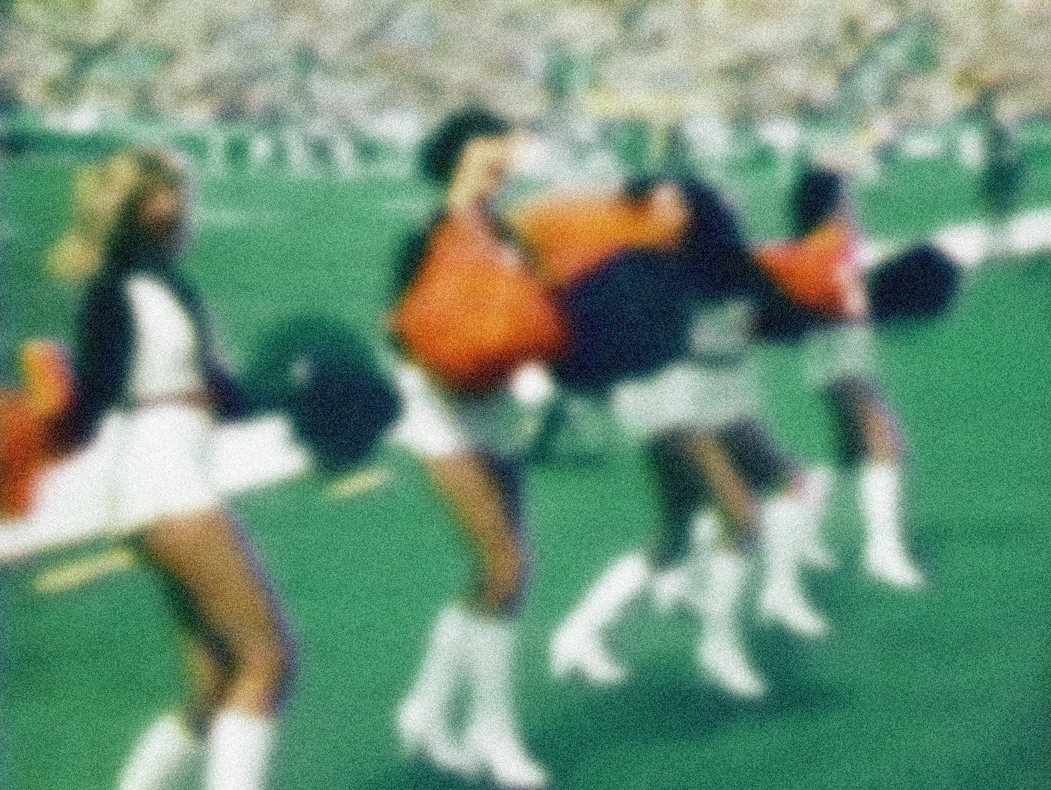 A group of football players sitting on a green field, wearing uniforms with black and white, and orange jerseys, holding helmets.