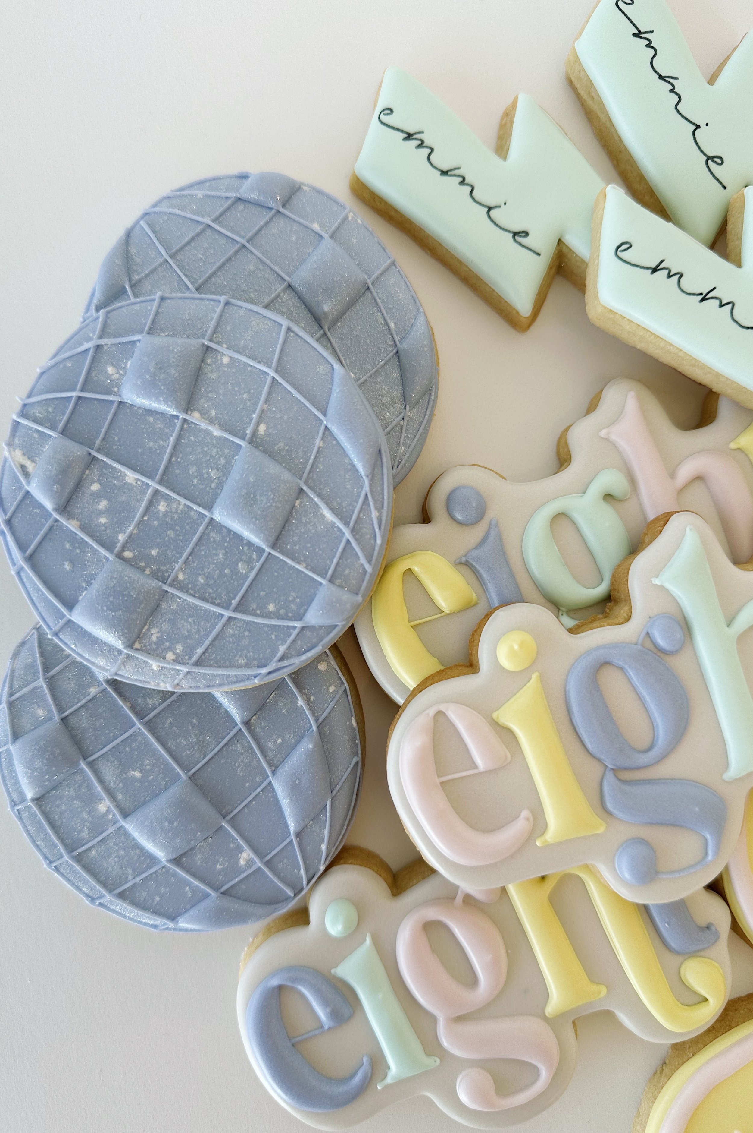 Decorative cookies shaped like the words 'enjoy' and 'celebrate', and three blue-colored eggs with a grid pattern.