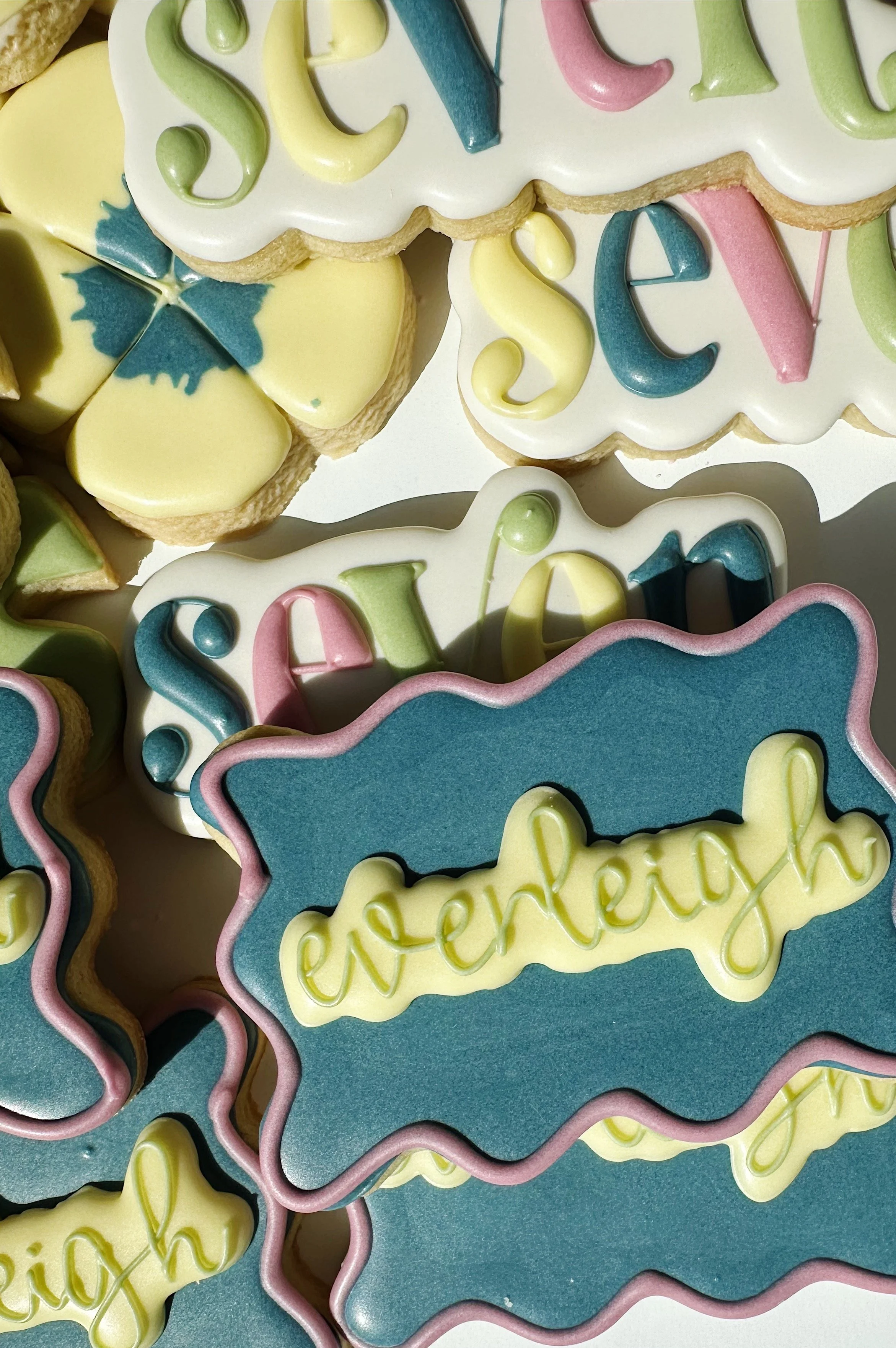 Colorful decorated cookies with messages like "celebrate" and "cherish," featuring pastel-colored icing, some with floral or abstract designs.