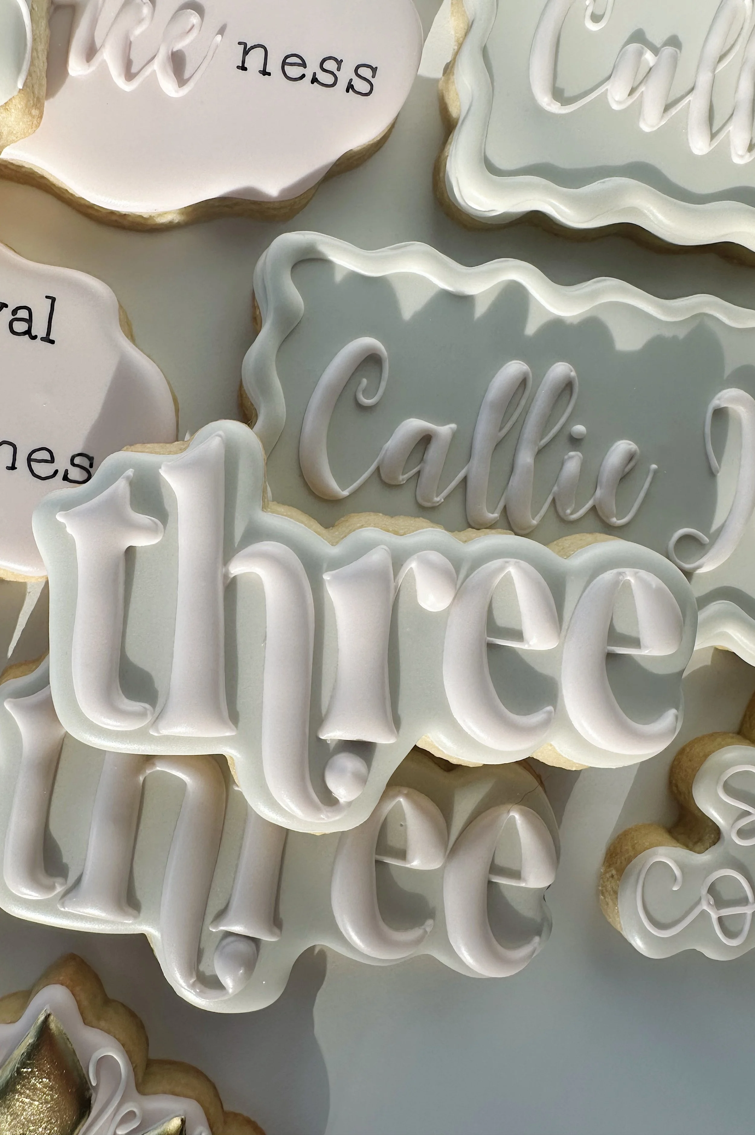 Assorted decorated sugar cookies with words like 'Callie' and 'thé' displayed on a white surface.