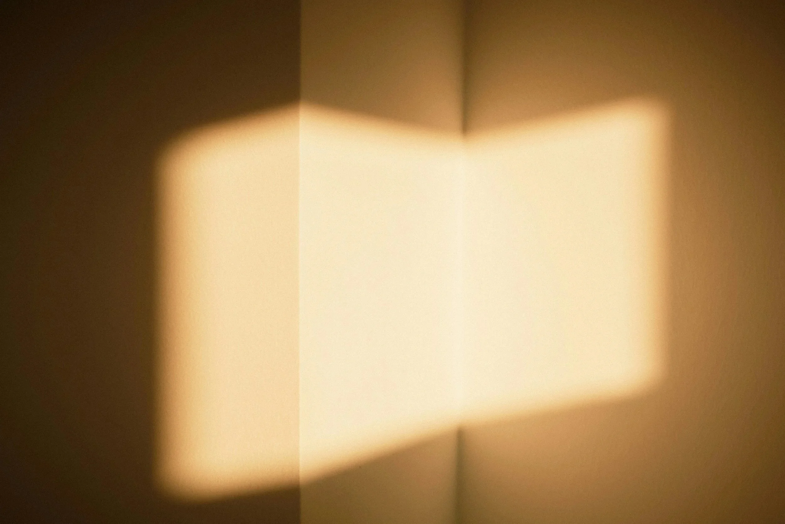 Abstract light pattern on a wall created by sunlight passing through a narrow opening.