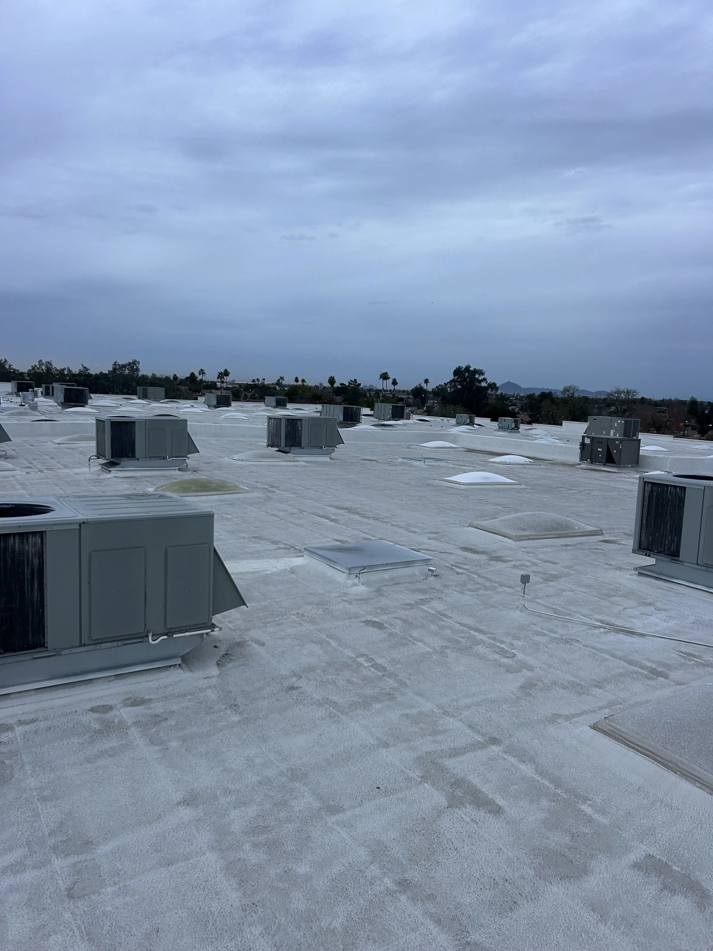 View of a flat roof with multiple HVAC units and vents, under a cloudy sky with distant trees and mountains.
