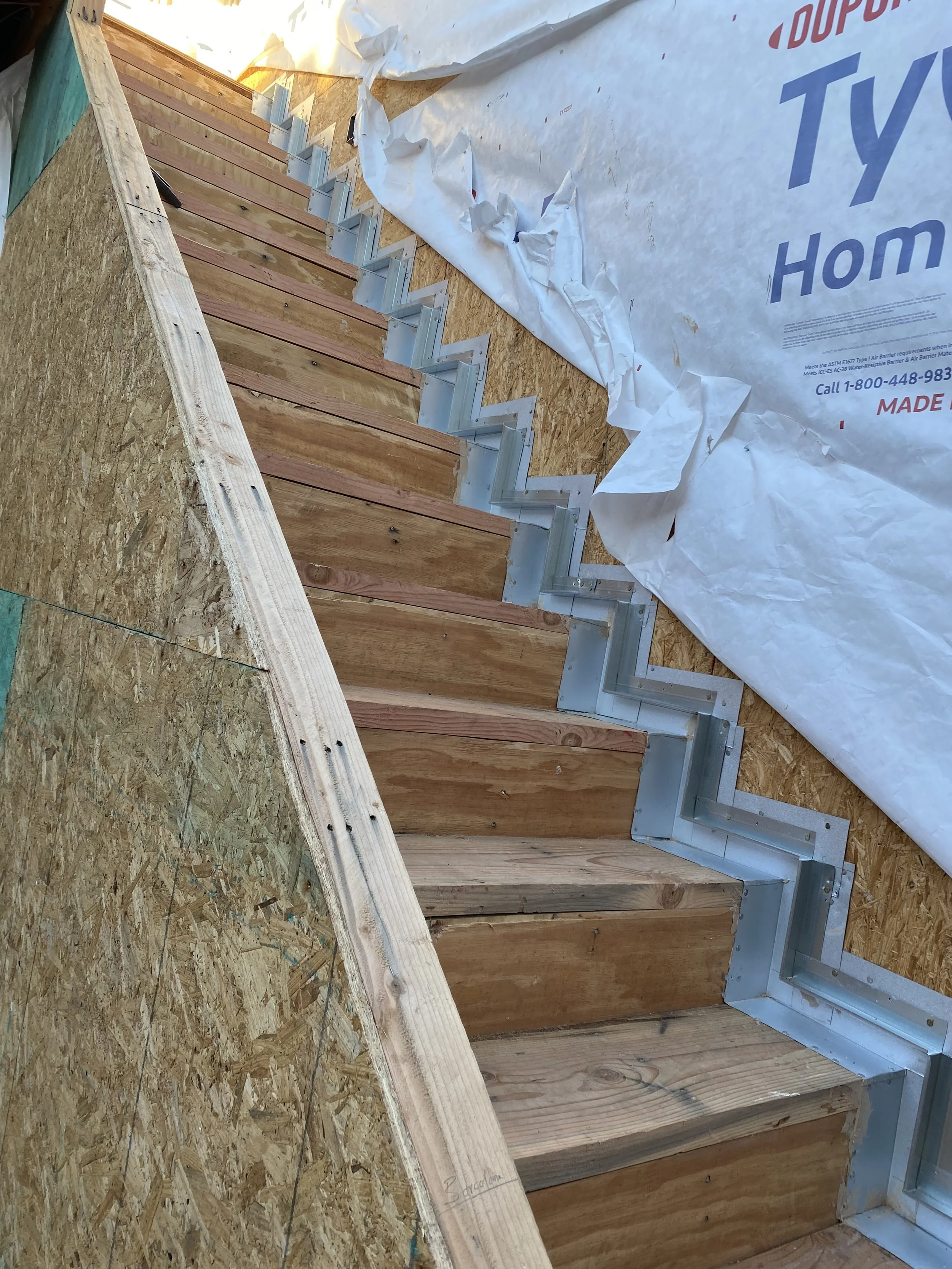 Wood framing with metal brackets for an interior staircase under construction, with building wrap around the area.