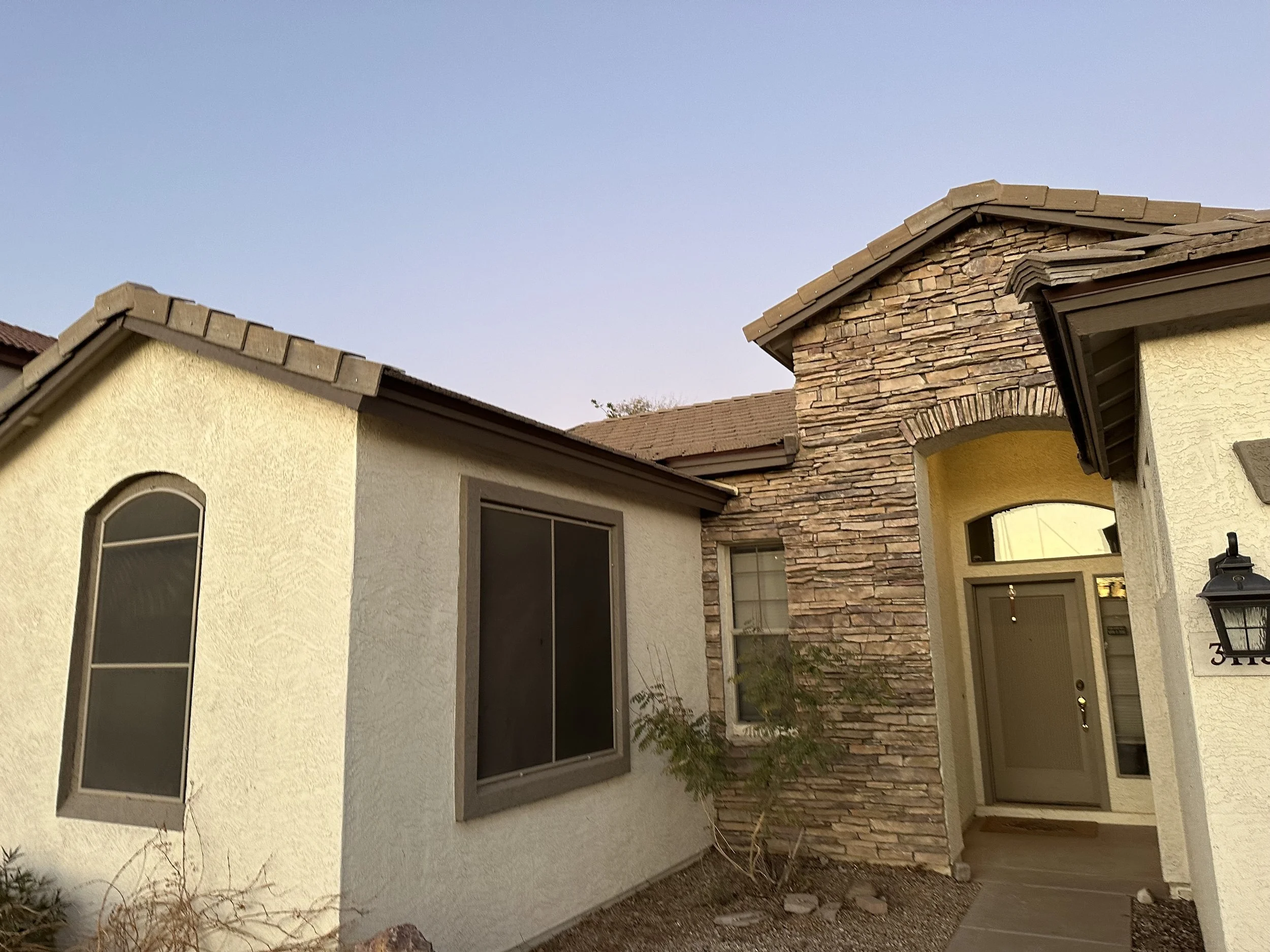 Front view of a house with a beige stucco exterior, a stone accent wall, arched windows, and a front door with a porch light.