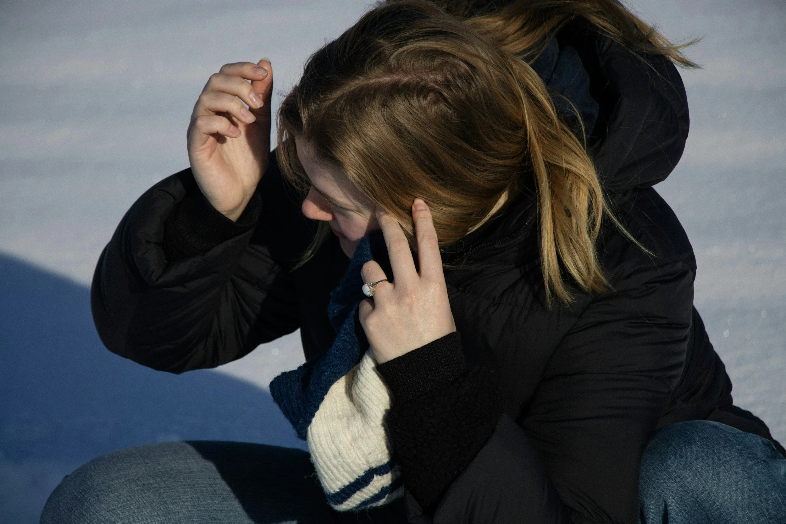 A woman sitting outdoors on snow, with her head bowed and hands on her face, appearing distressed or upset.