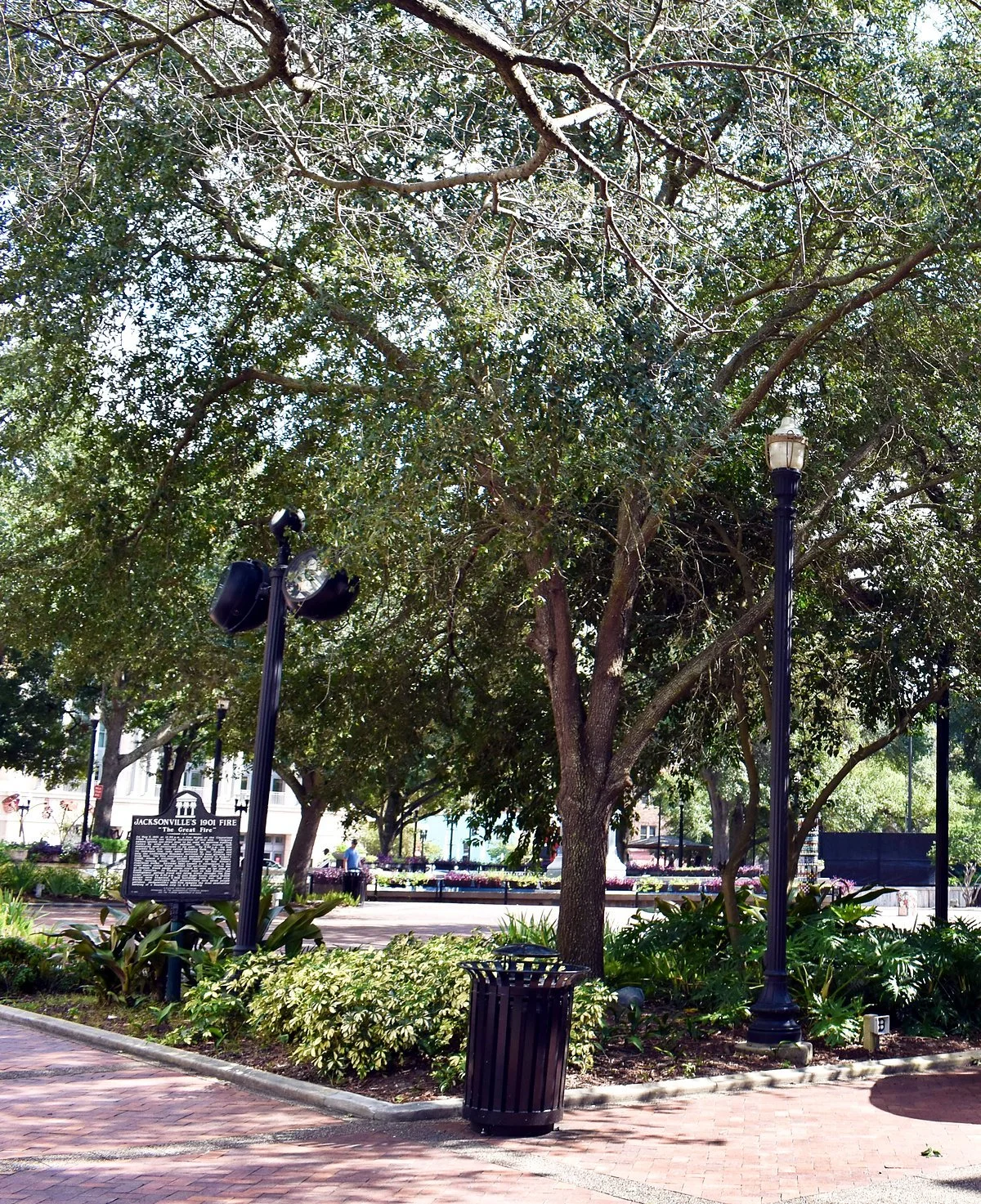 Shaded brick walkway, planted beds, and street lamps in a downtown Jacksonville park