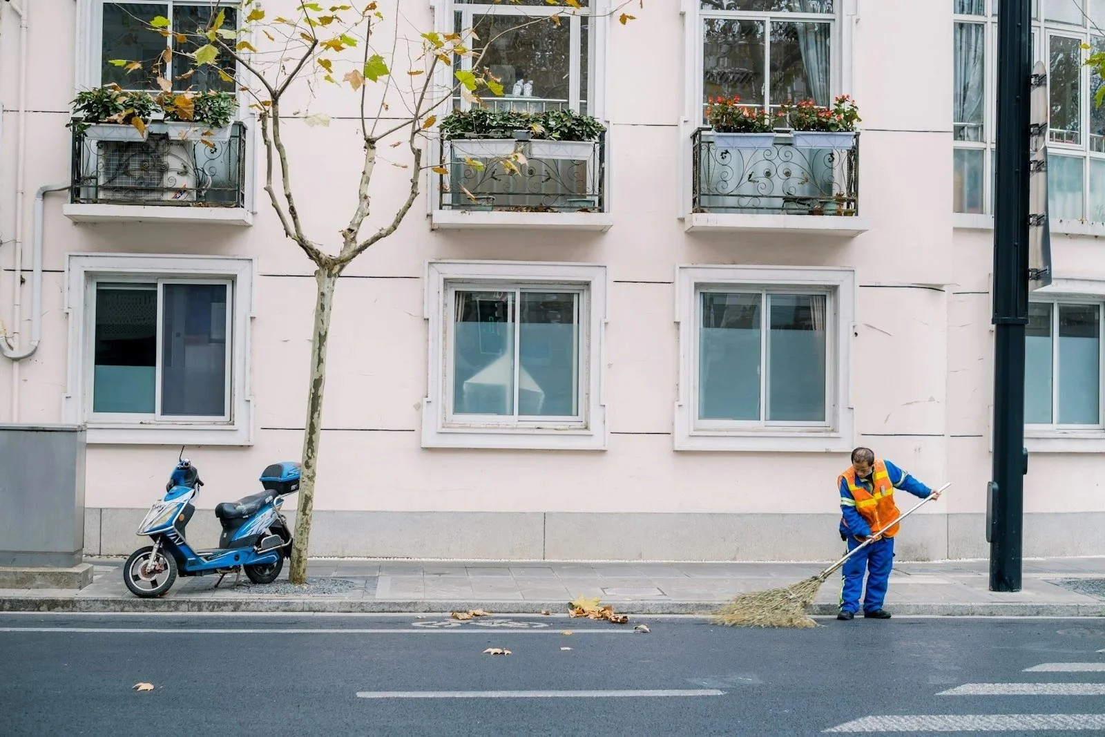 Suncatcher porter sweeping leaves from the curb in front of a commercial building