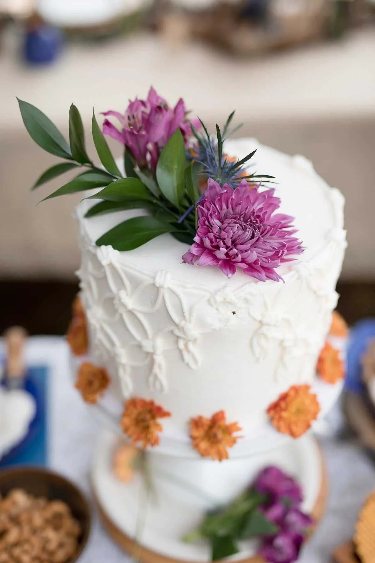 A white cake decorated with pink, purple, and orange flowers and green leaves.