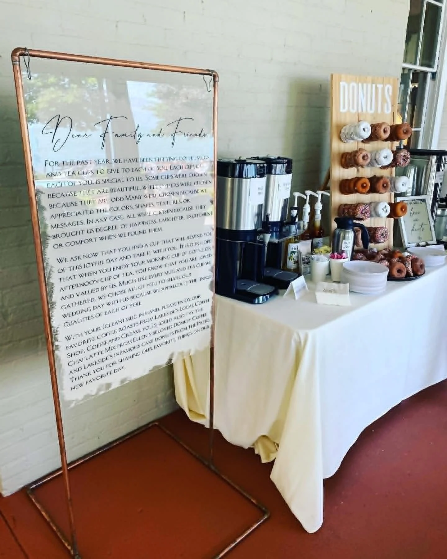 Sign with a message to family and friends, and a table with coffee, cups, and a display of donuts on a wooden board labeled 'DONUTS'.