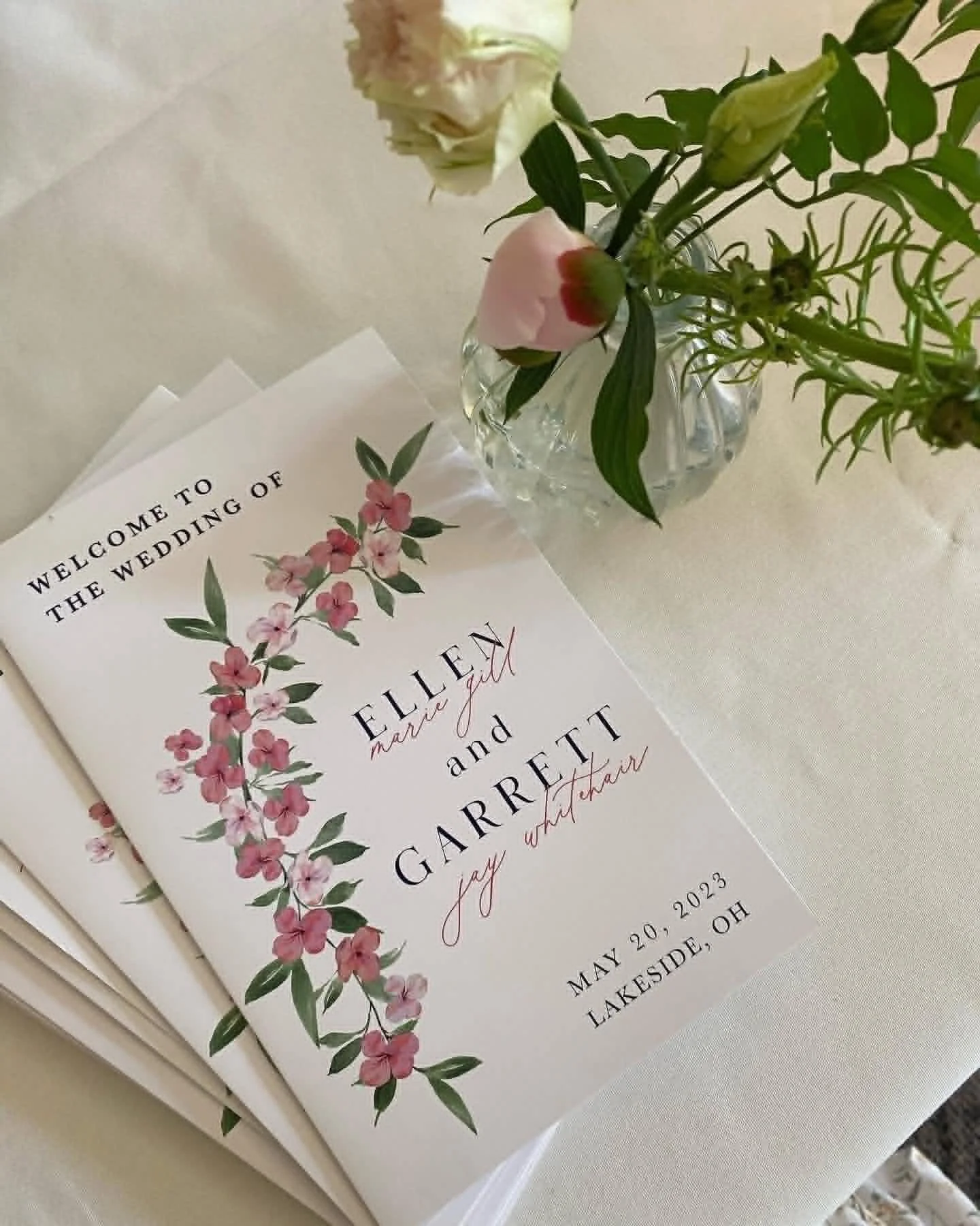Wedding invitation with floral design, featuring pink and green accents, on a white surface.