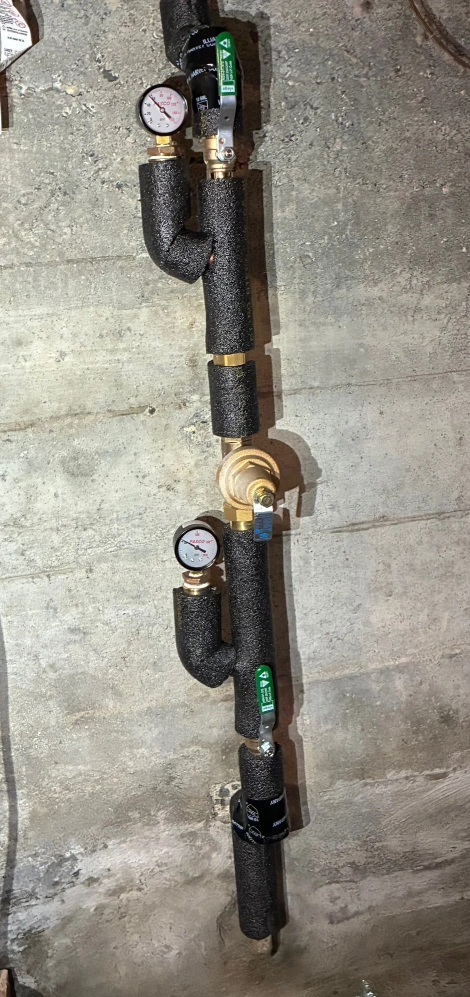 A plumbing pipe system with insulated pipes, gauges, and valves installed on a concrete wall.