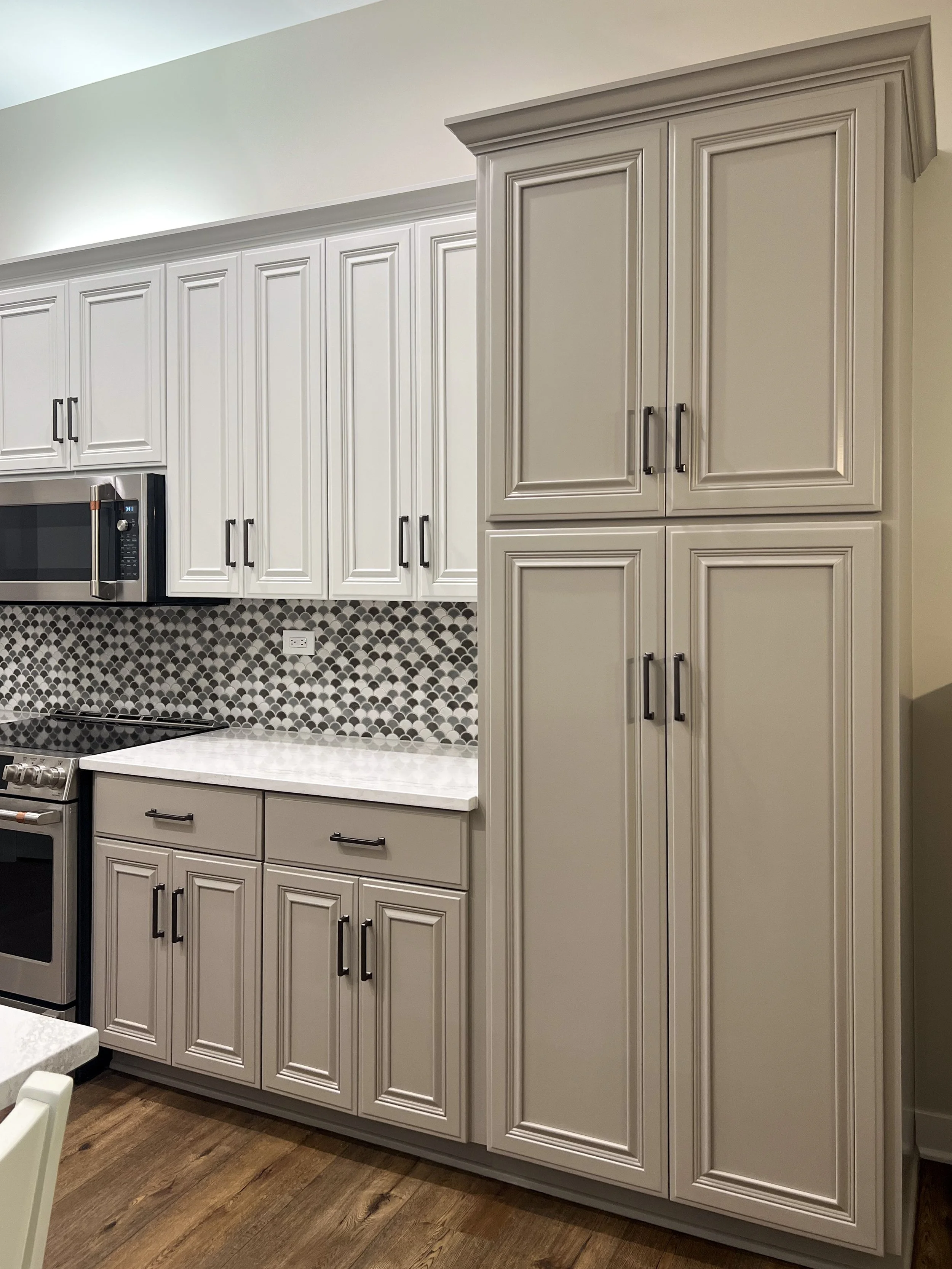 Kitchen with white cabinetry, black handles, a patterned backsplash, stainless steel microwave, stove, and a hardwood floor.