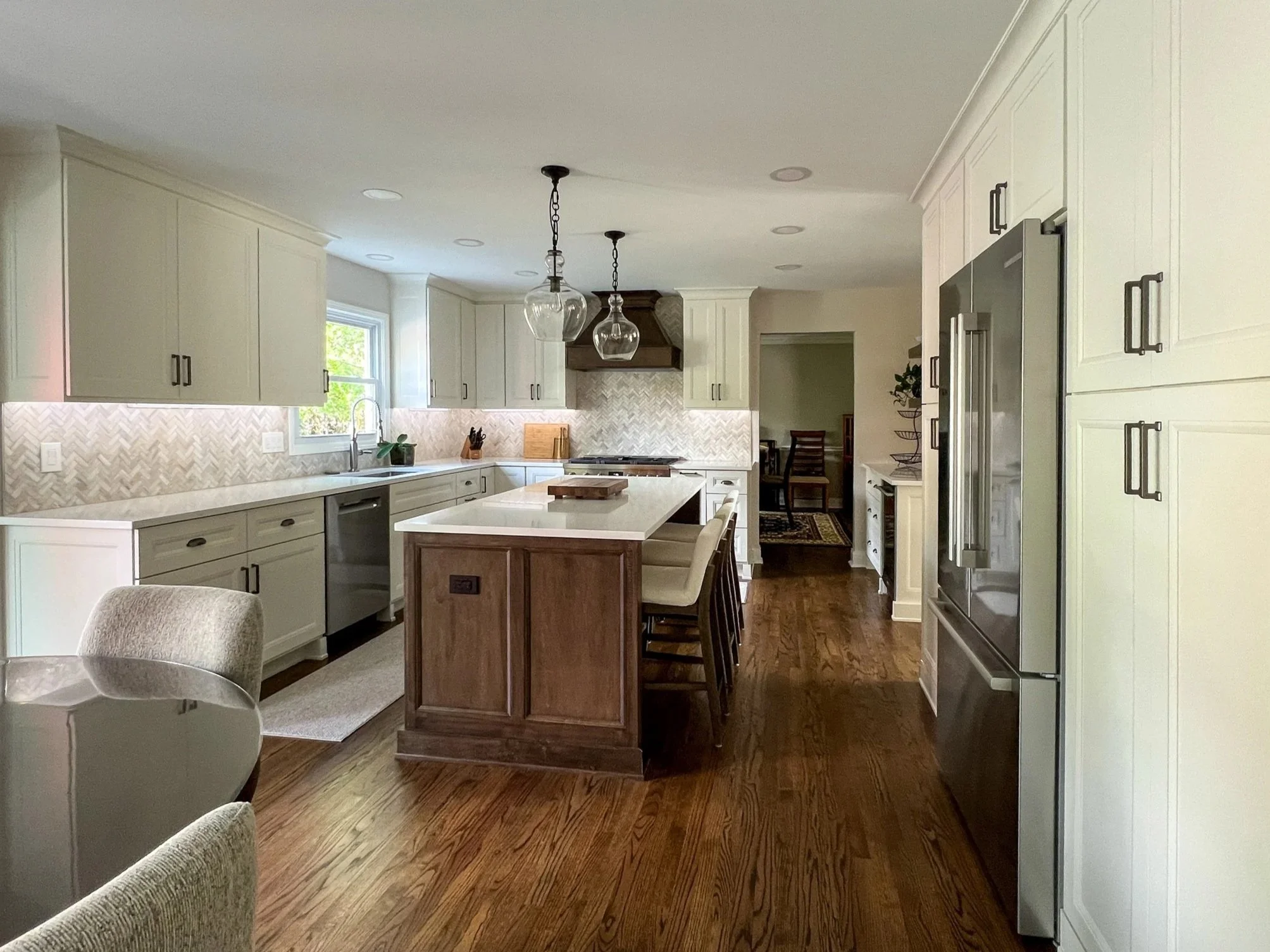 Modern kitchen with white cabinets, a kitchen island, pendant lights, hardwood floors, and a stainless steel refrigerator.