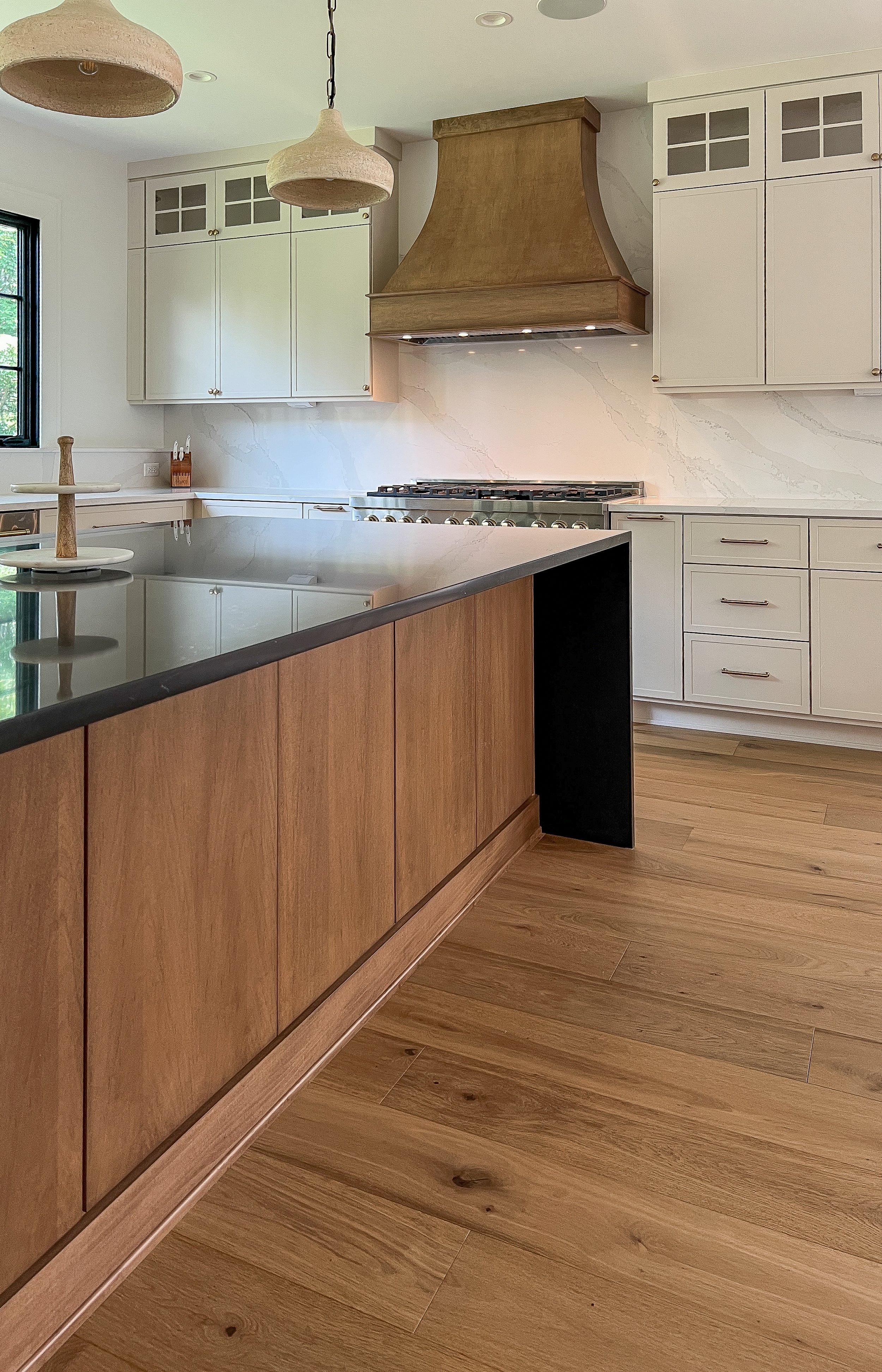 Modern kitchen with white cabinetry, wooden accents, a large island with black countertop, a stove with a wooden range hood, and hardwood floors.