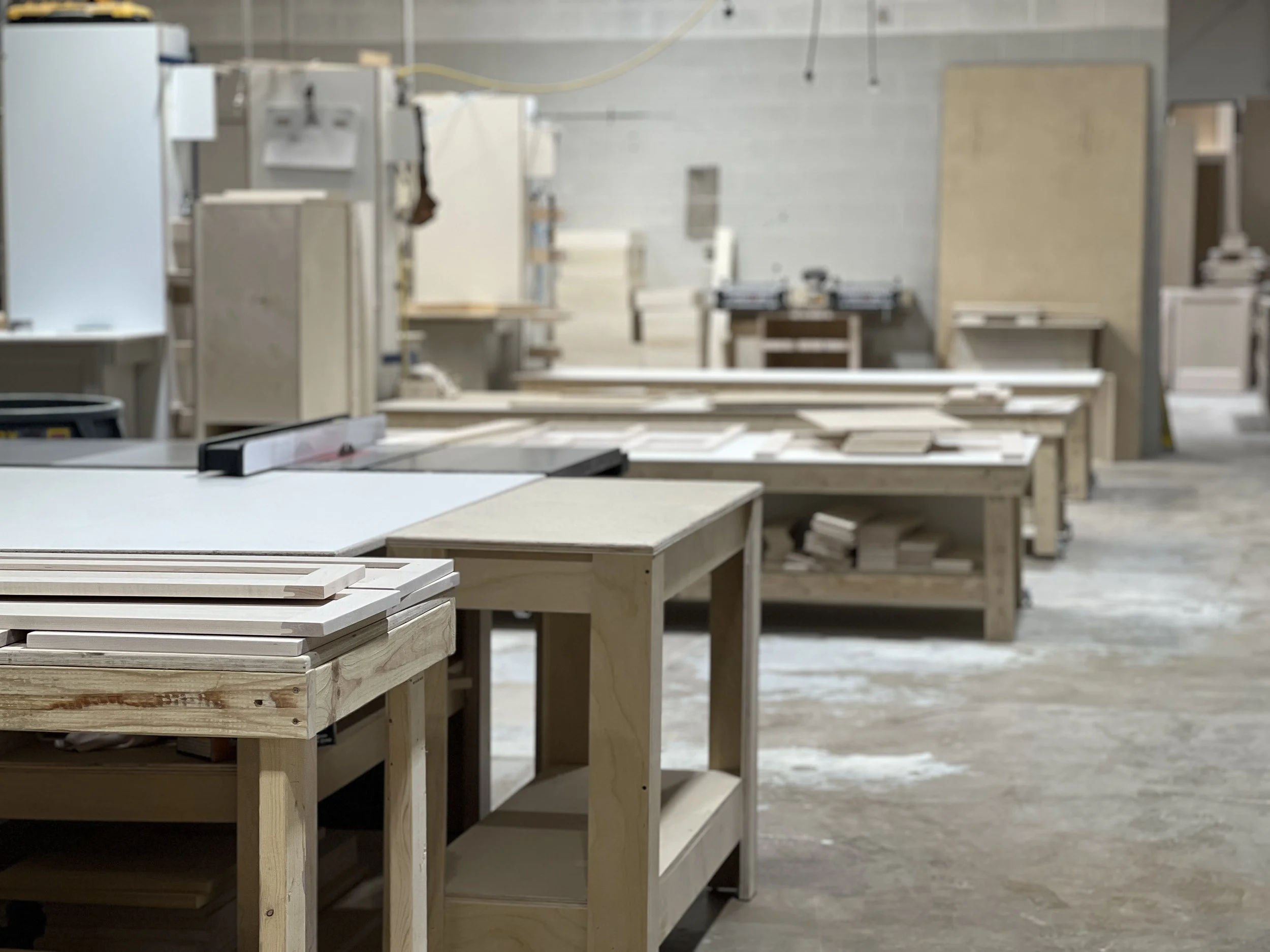Woodworking workshop with tables and materials, unfinished wood pieces, and tools in the background.