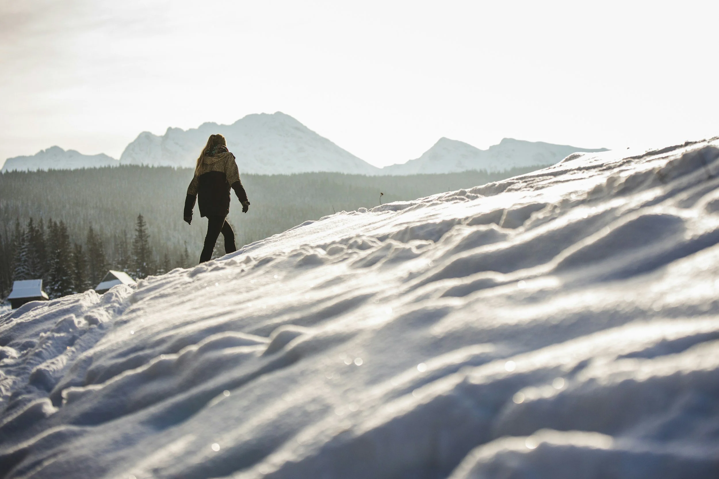 Person walking through snowy landscape with snow-covered mountains in the background.