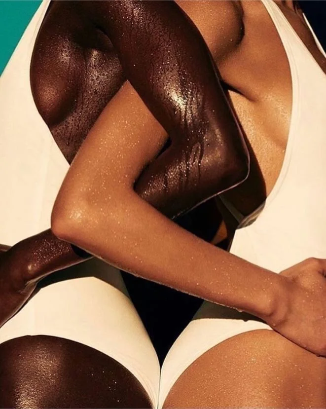 Close-up of two intertwined arms, one dark-skinned and one light-skinned, both glistening with moisture, and part of their clothing visible.