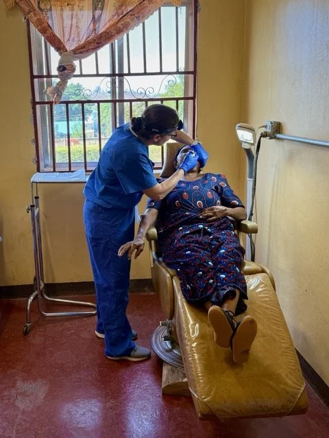 A nurse attending to a patient lying on a hospital bed in a brightly lit room, with a window showing outdoor scenery.