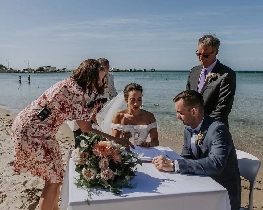 Married by Beck - Melbourne and Mornington Peninsula celebrant is in Sorrento at The Baths with people signing marriage papers on a beach, with the ocean in the background.