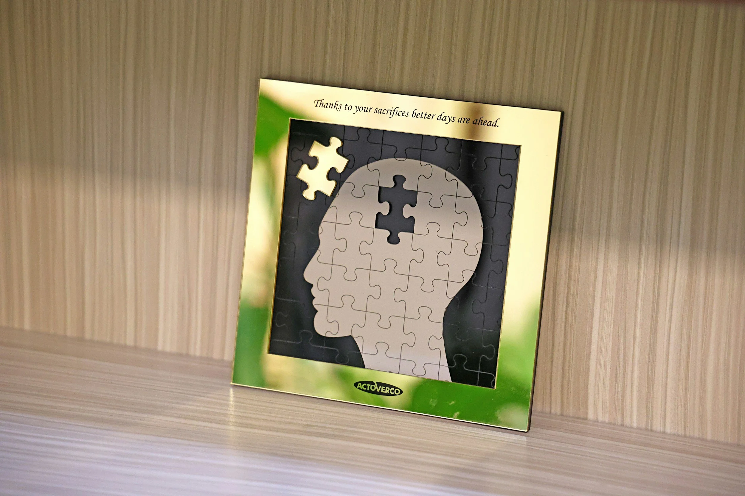 A jigsaw puzzle of a human head profile with a missing piece in the brain area, set on a shelf against a striped wall, with a message about better days ahead.