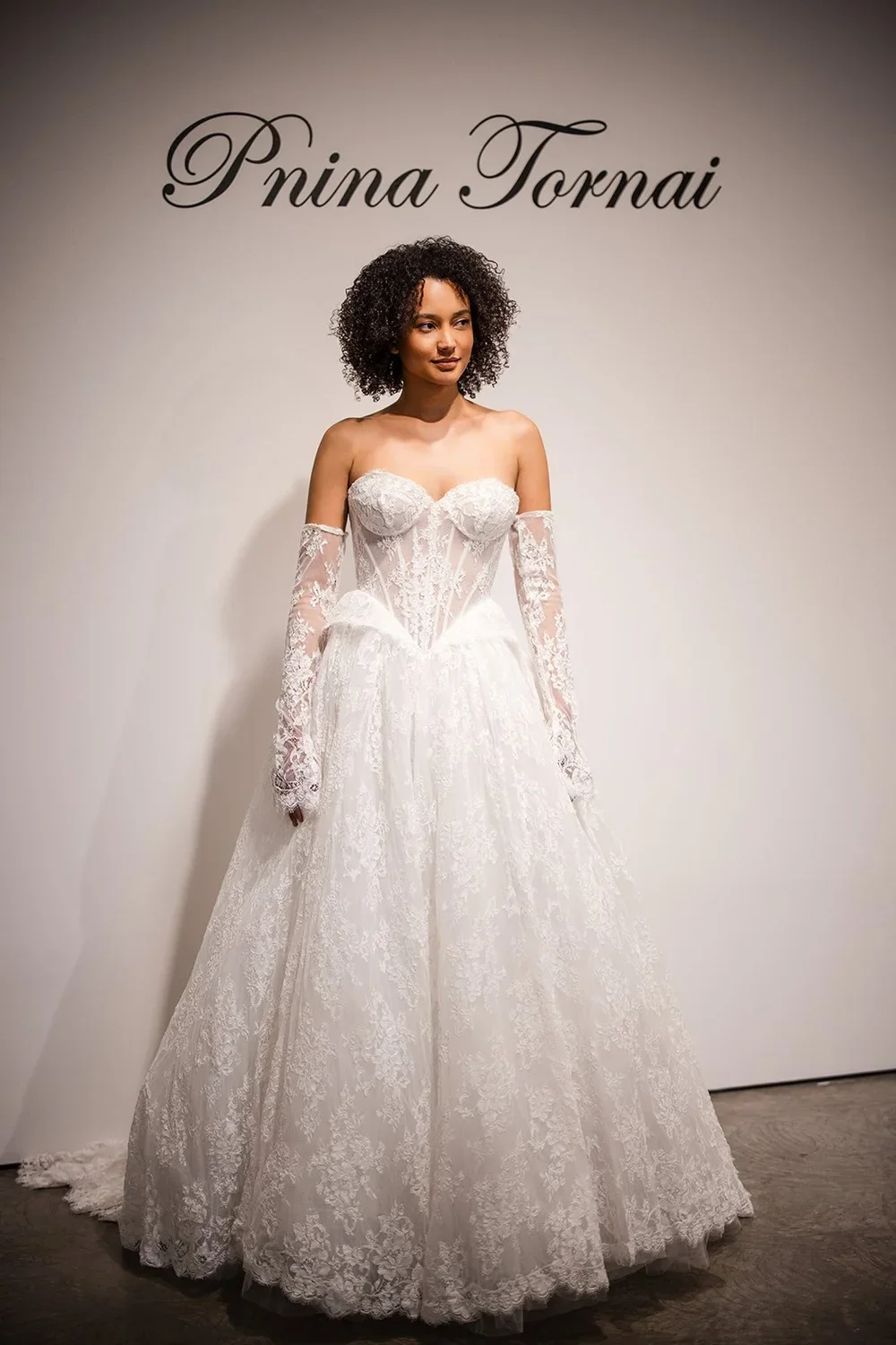A woman trying on a wedding dress at a boutique with designer Pnina Tornai's name on the wall behind her.