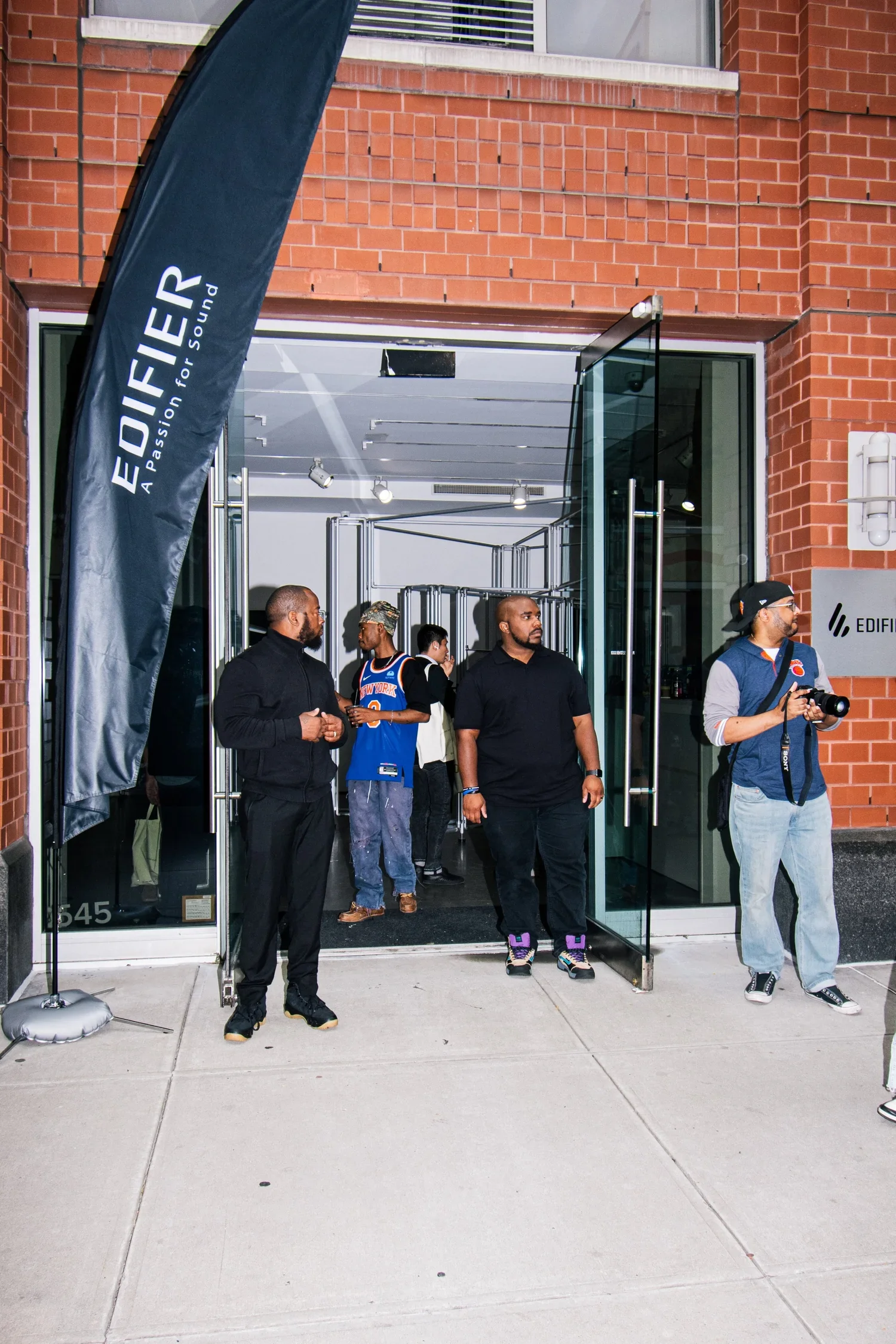 People standing outside the entrance of a building with a black flag that says 'EDIFIER' and 'A Passion for Sound.'