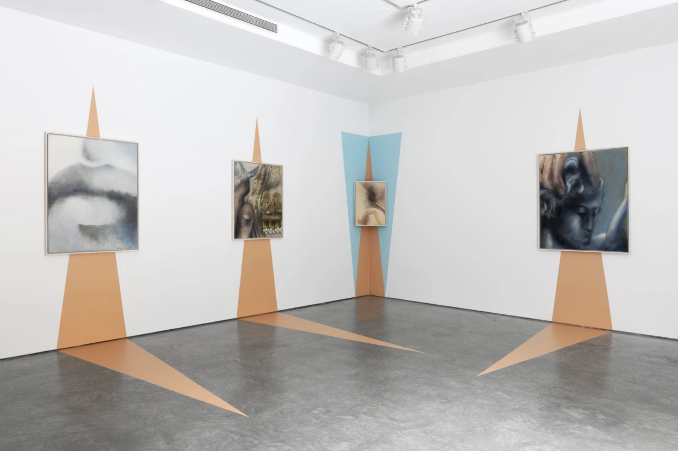 Art gallery with five framed paintings on white walls decorated with geometric shapes in orange and blue, and spotlights on the ceiling.