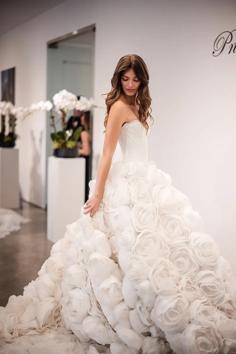 A woman in a wedding dress with a long skirt made of large white roses in a bridal boutique.