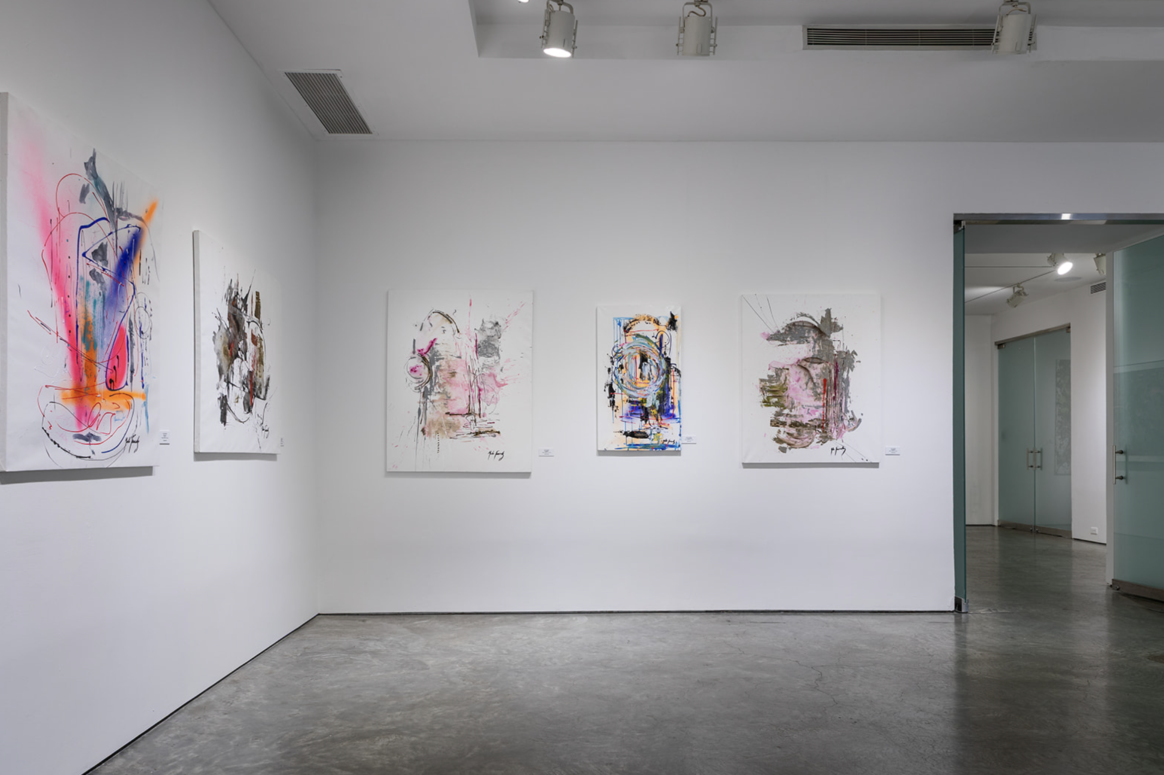 Gallery wall displaying five abstract paintings with various colors and brushstrokes in an art gallery with white walls and concrete floor.