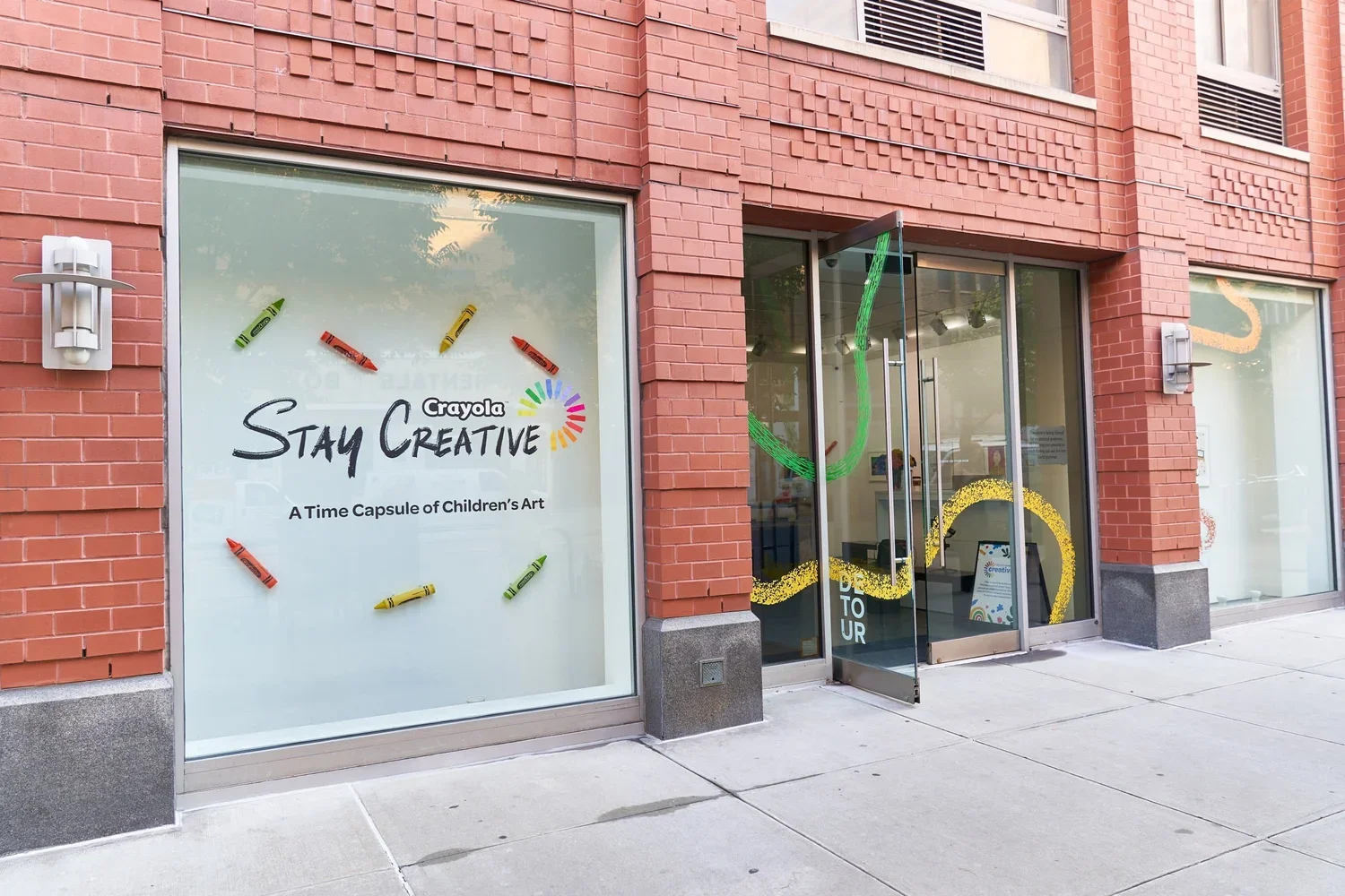 Store window with Crayola branding, decorated with colorful crayon graphics and the message 'Stay Creative,' promoting children's art.