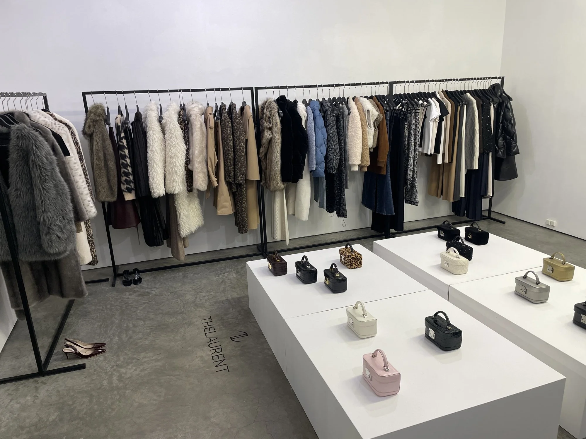 Clothing racks with various coats and jackets, and display tables with handbags in a fashion store.