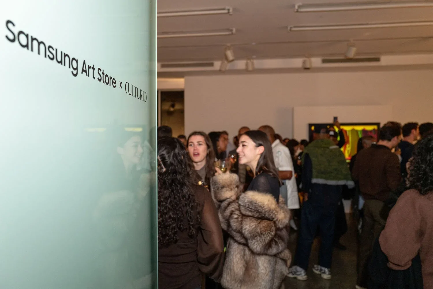 People gather at the Samsung Art Store x (CULTURE) event in an indoor gallery with white walls and ceiling-mounted lights, engaging in conversations.