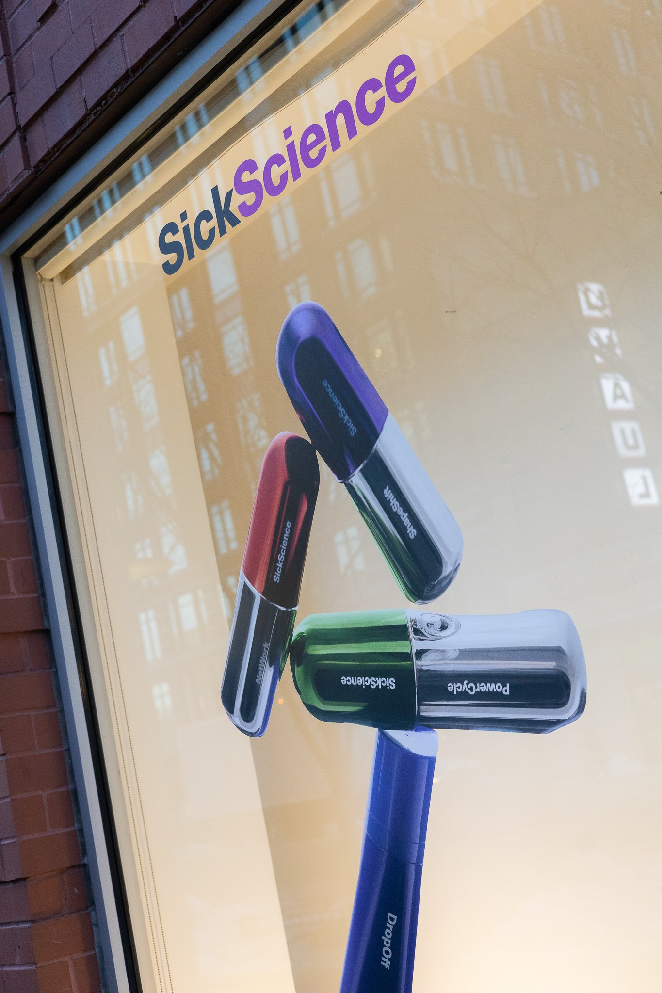 A window display shows a sign for SickScience with three connected capsules, each labeled with 'SickScience' or related words, and a blue baton labeled 'DropOff' holding the capsules.