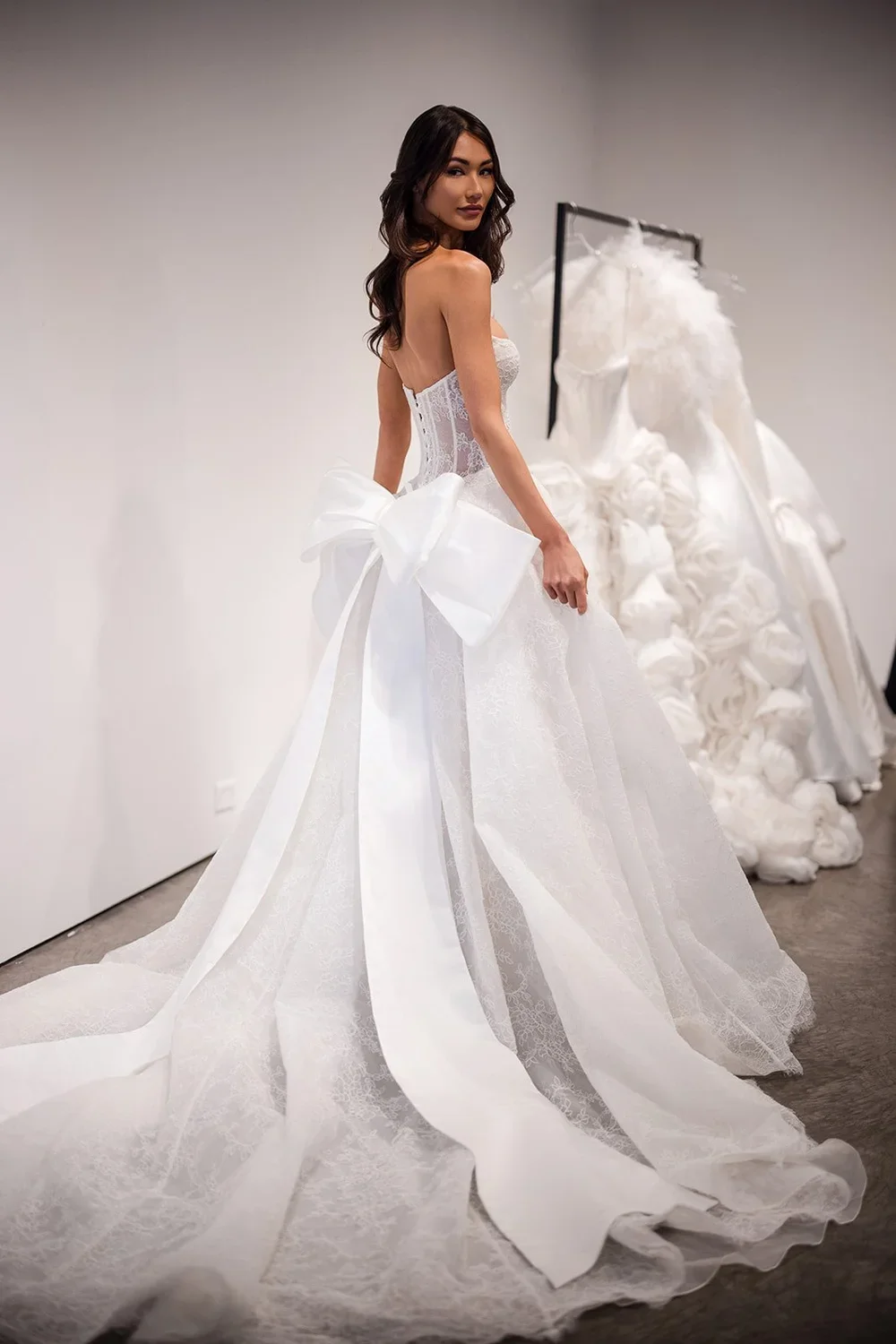 A woman trying on a wedding dress with a large bow on the back inside a bridal shop.