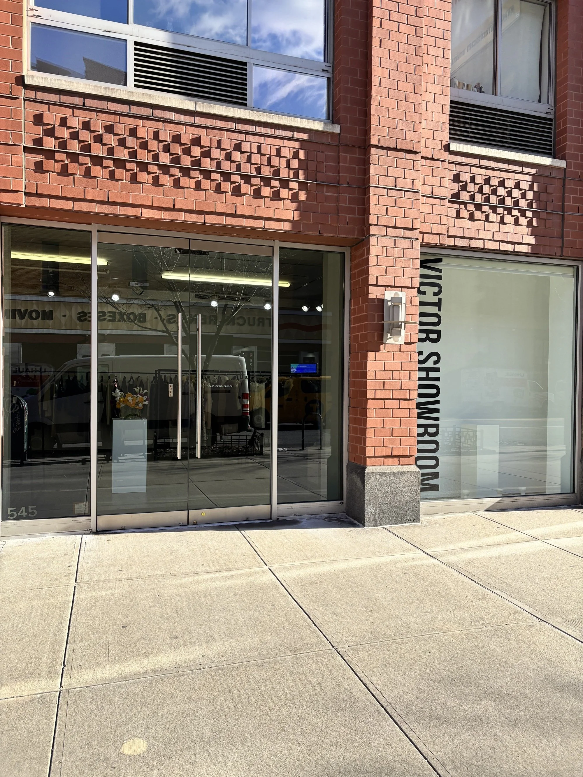 Storefront with large glass doors and windows branded with 'VICTOR SHOE ROOM', brick exterior, sidewalk in front, and reflections of cars and buildings.
