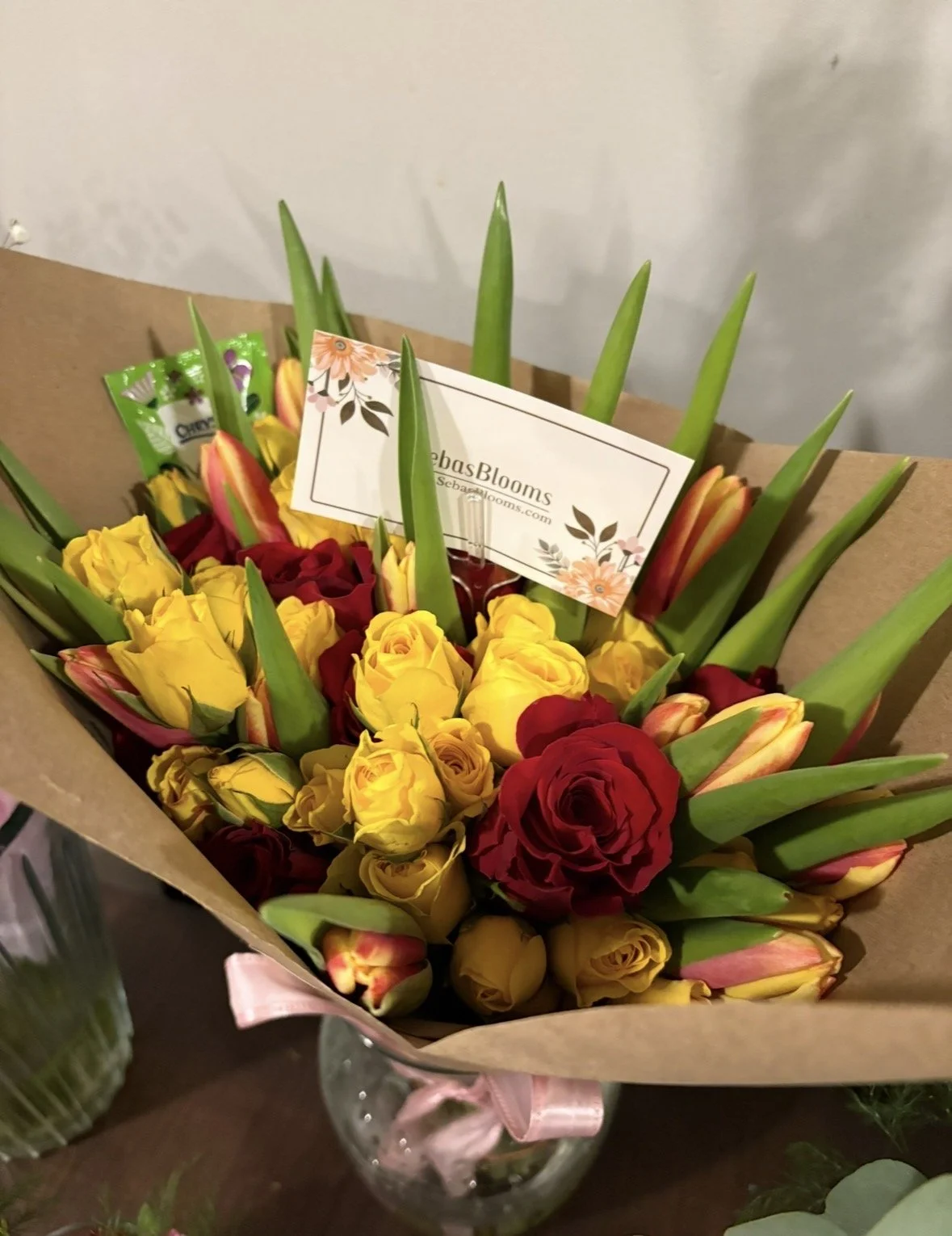 Bouquet of yellow and red roses with green leaves and a business card from SebasBlooms.