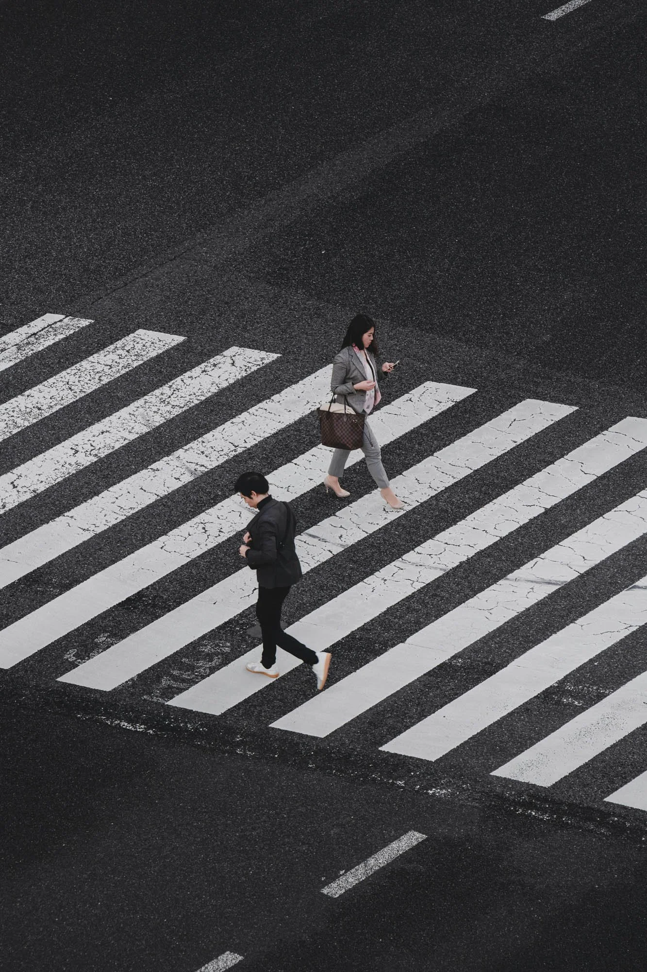Overhead view of three pedestrians crossing a street with painted crosswalk lines.
