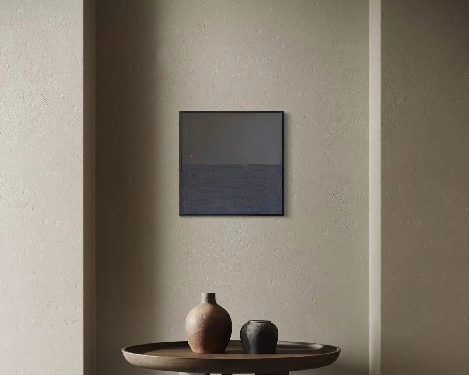 A beige wall decorated with a framed picture, placed above a wooden table holding three vases of different sizes and colors.