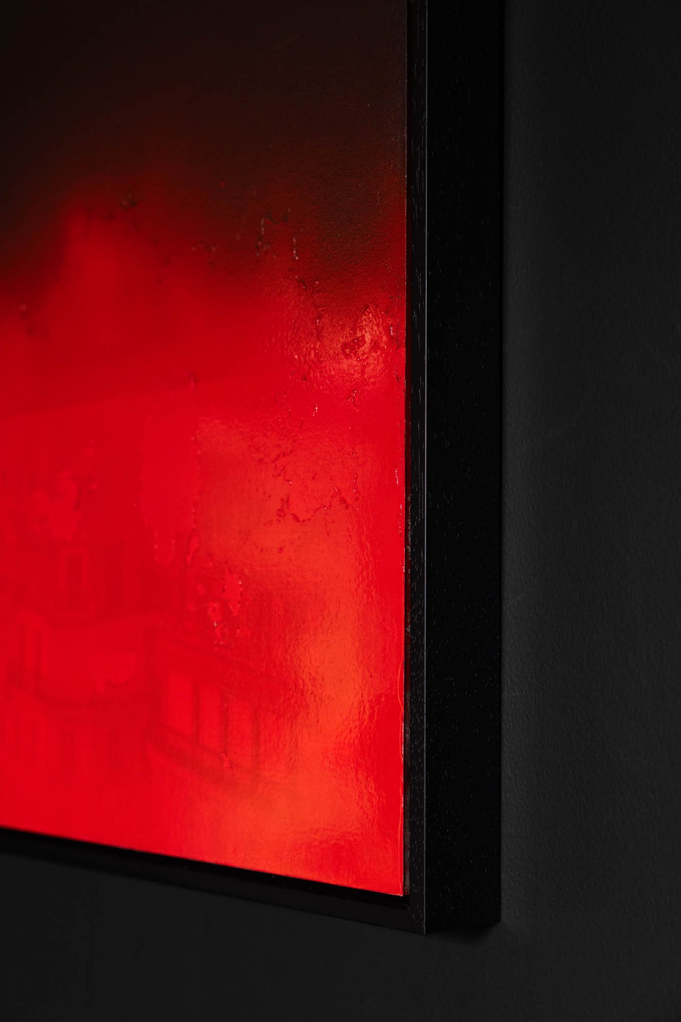 Close-up of a black frame holding a red artwork or panel, with a textured surface and black background.