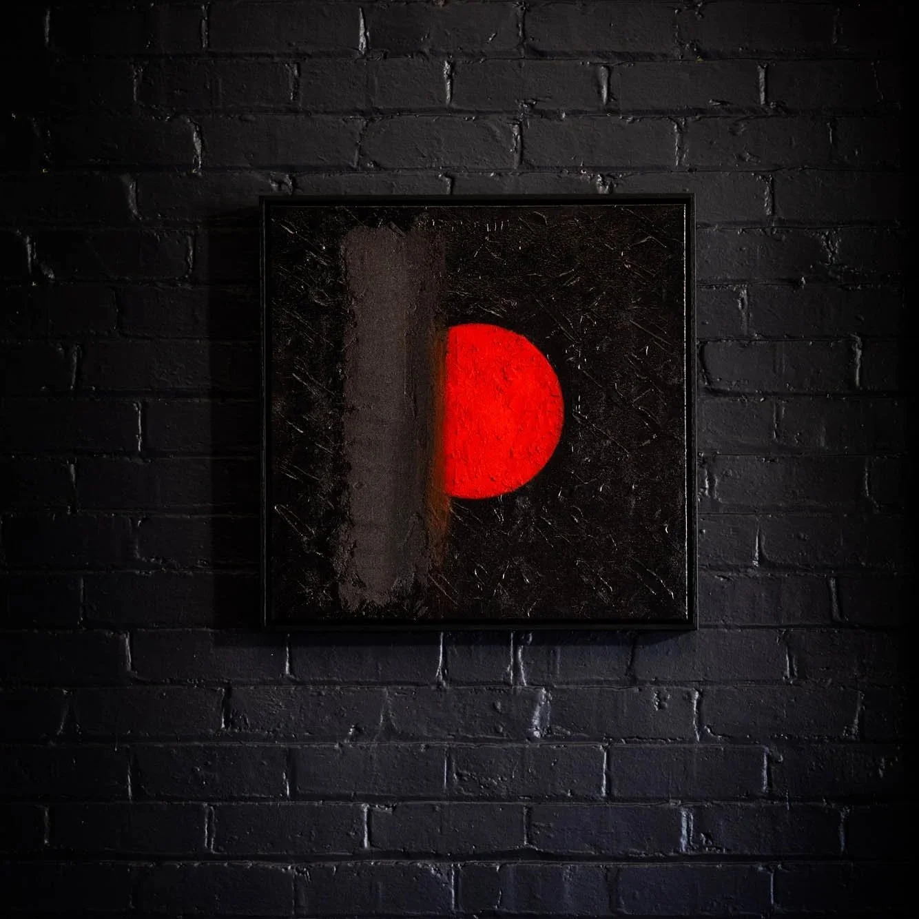 Abstract artwork of a red semi-circle on black textured background, framed on a black brick wall.