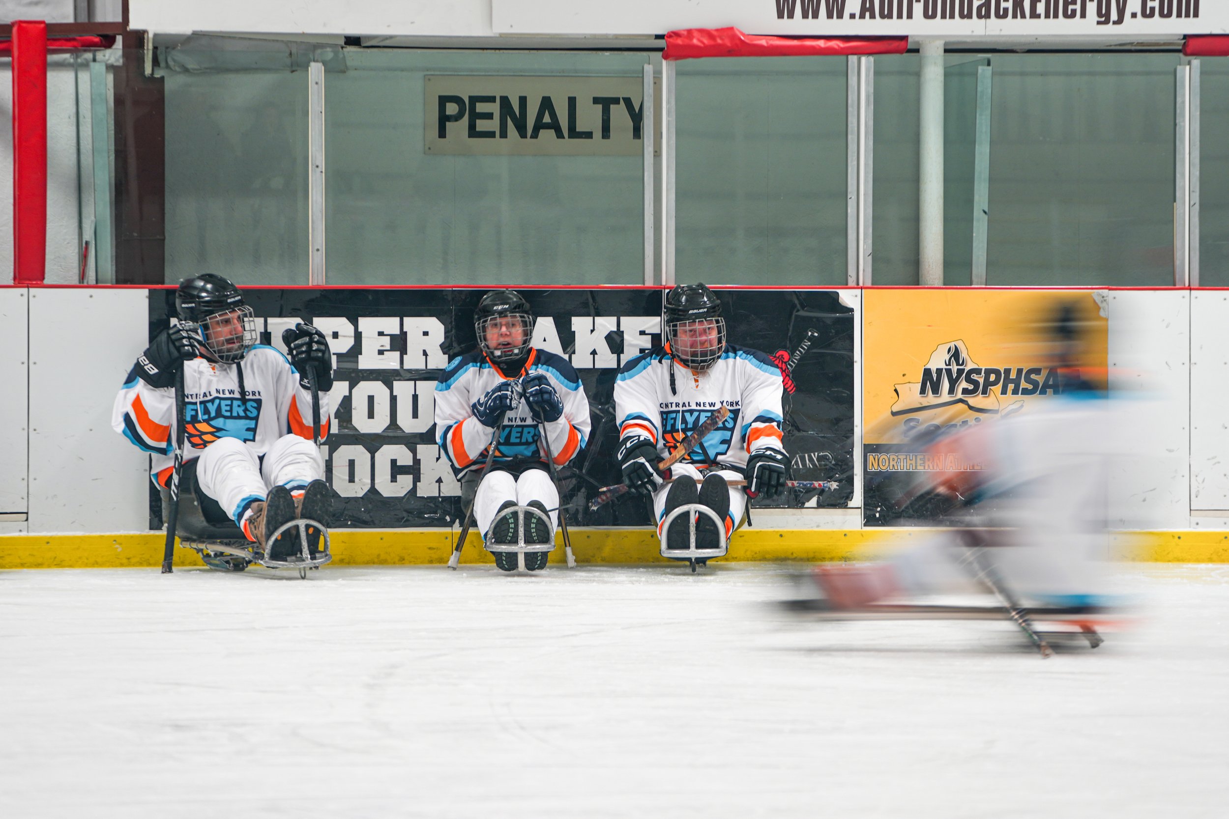 CNY Flyers forwards watch as a teammate speeds past during their game vs Capital District Sled Warriors on February 6, 2026 at the Tupper Lake Civic Center in Tupper Lake, NY. (Isaac Williams/The Newhouse School)