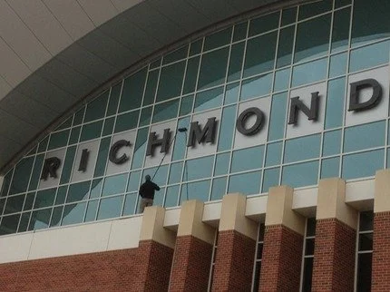 Window cleaner on building cleaning large sign that says "RICHMOND" with brick and glass facade.