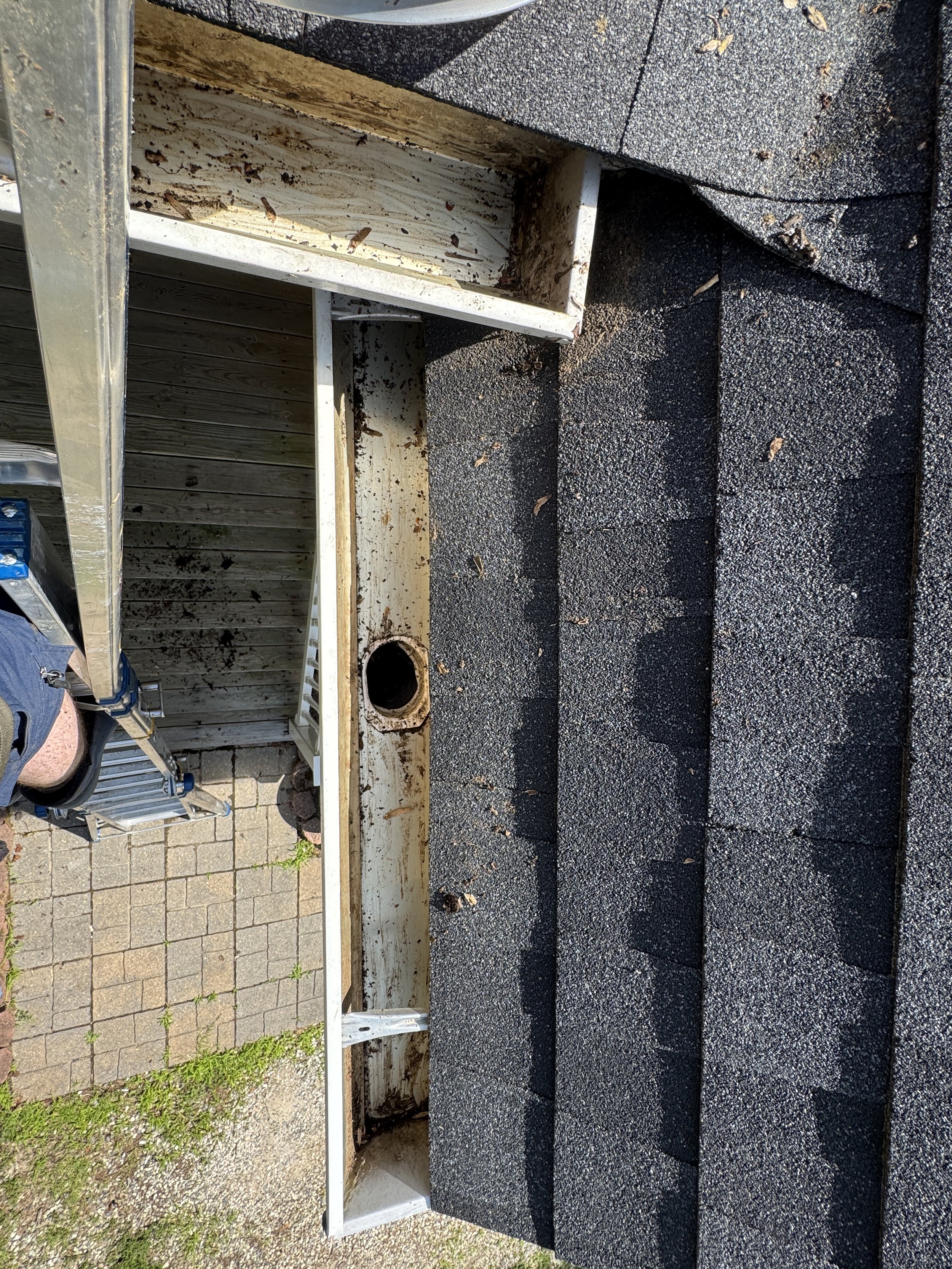 Empty metal and wooden storage shelf attached to the roof of a building, with a black gravel surface underneath and some small green plants growing nearby.