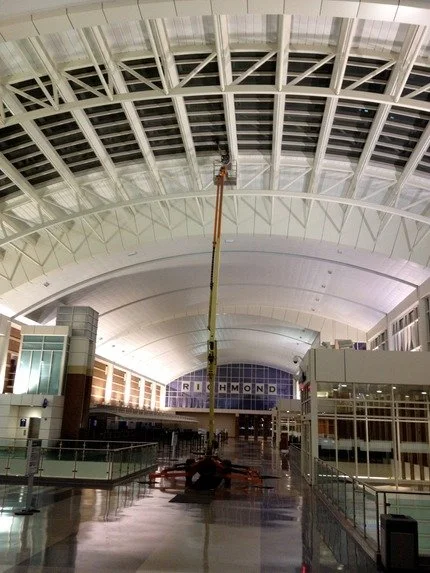 Construction worker on a boom lift working on the ceiling of a large, modern airport terminal.