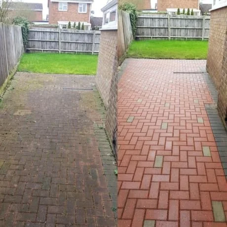 Side-by-side comparison of a driveway showing before and after cleaning and renovation, with a wooden fence and houses in the background.