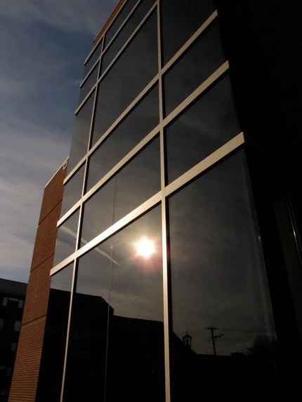 Modern building with large glass windows reflecting sunlight and partly cloudy sky.